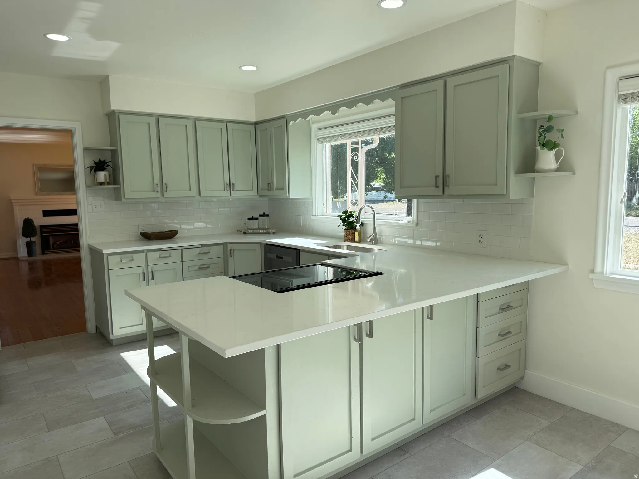 Kitchen featuring light green cabinetry, white subway tile backsplash, light-toned countertops, and an integrated cooktop