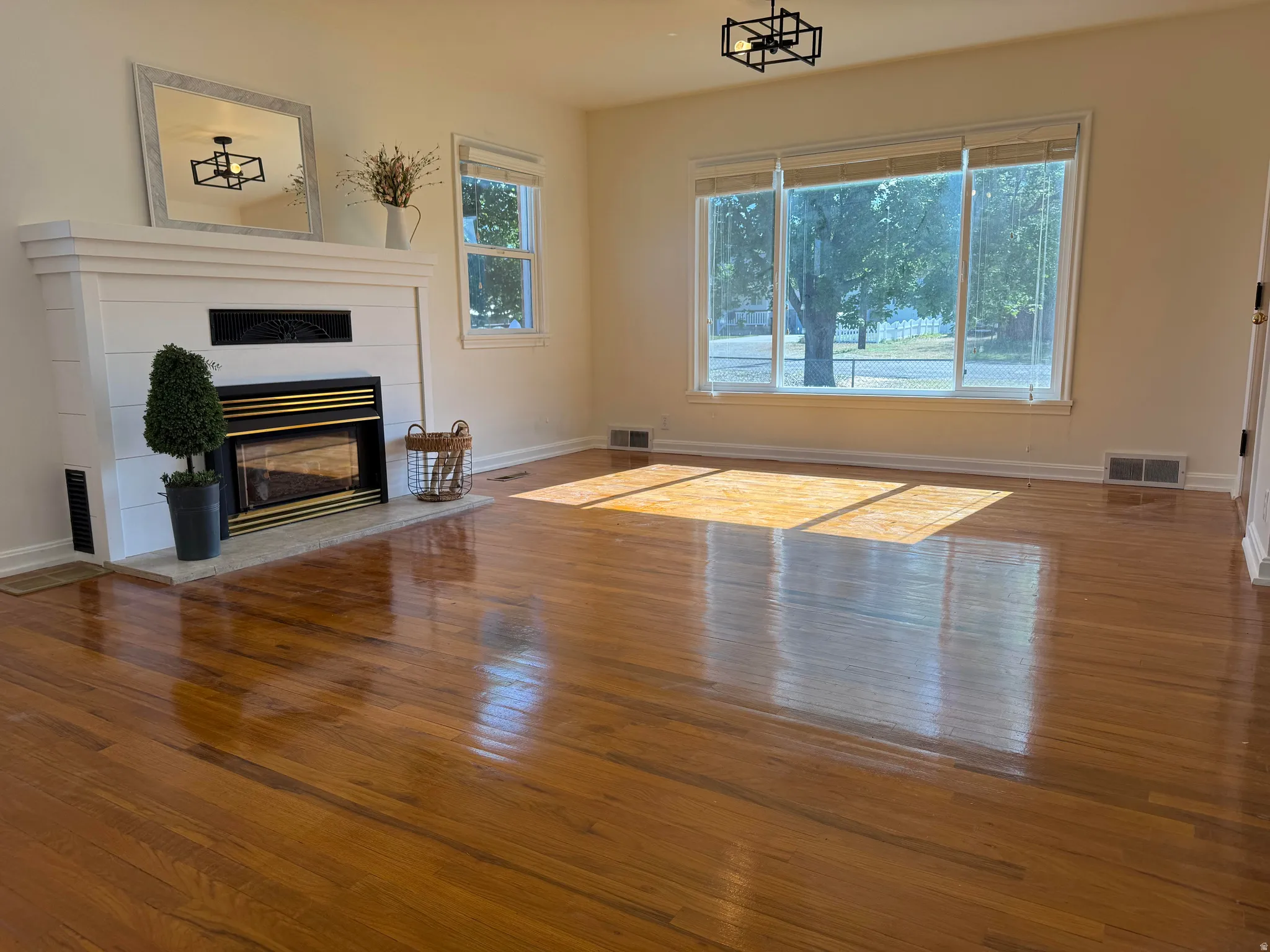 Spacious room featuring polished wood flooring, a fireplace with a white shiplap-style mantel, and a large picture window