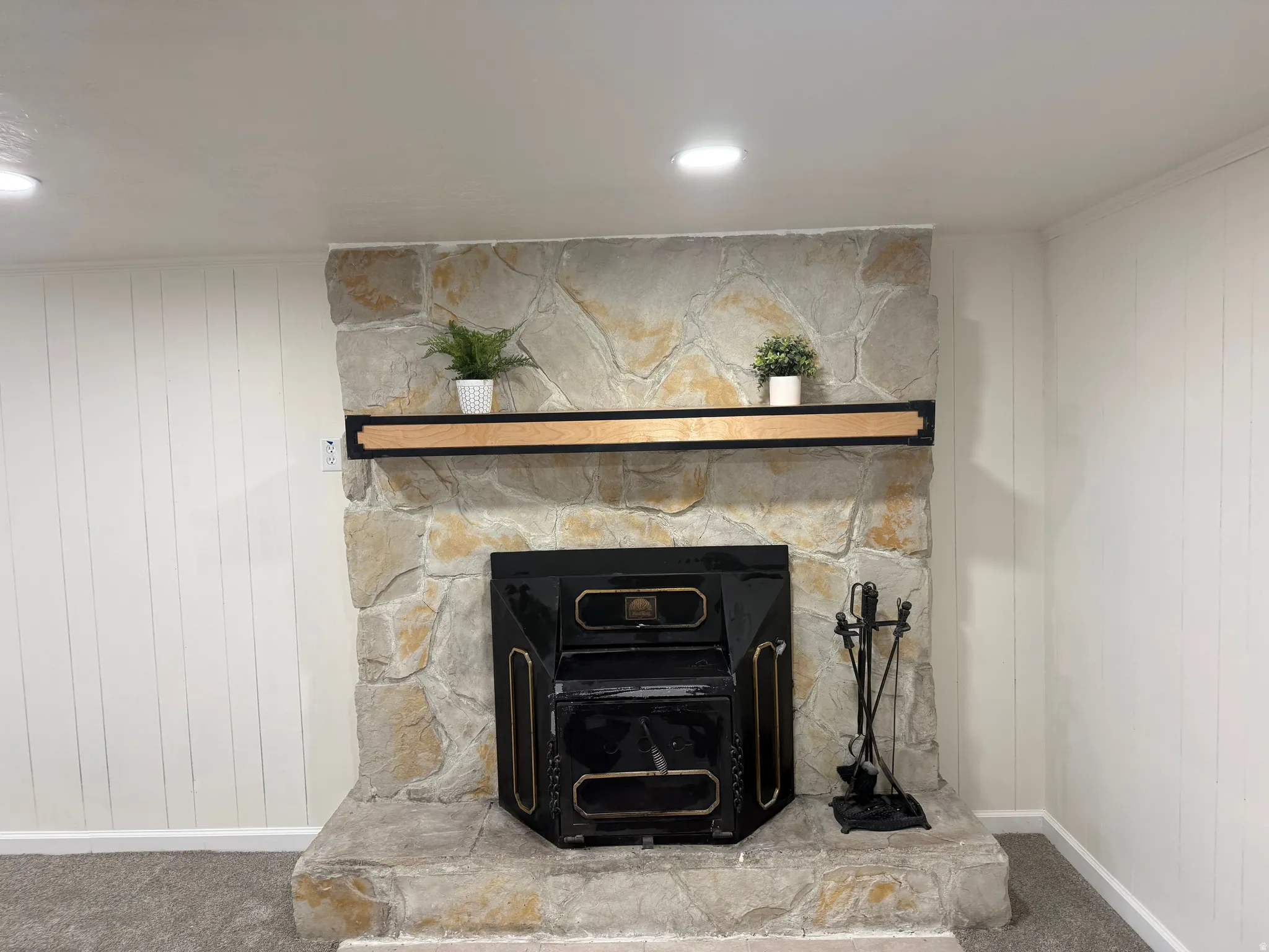 Stone fireplace featuring a black metal fireplace insert, a wood mantel, and a stone hearth