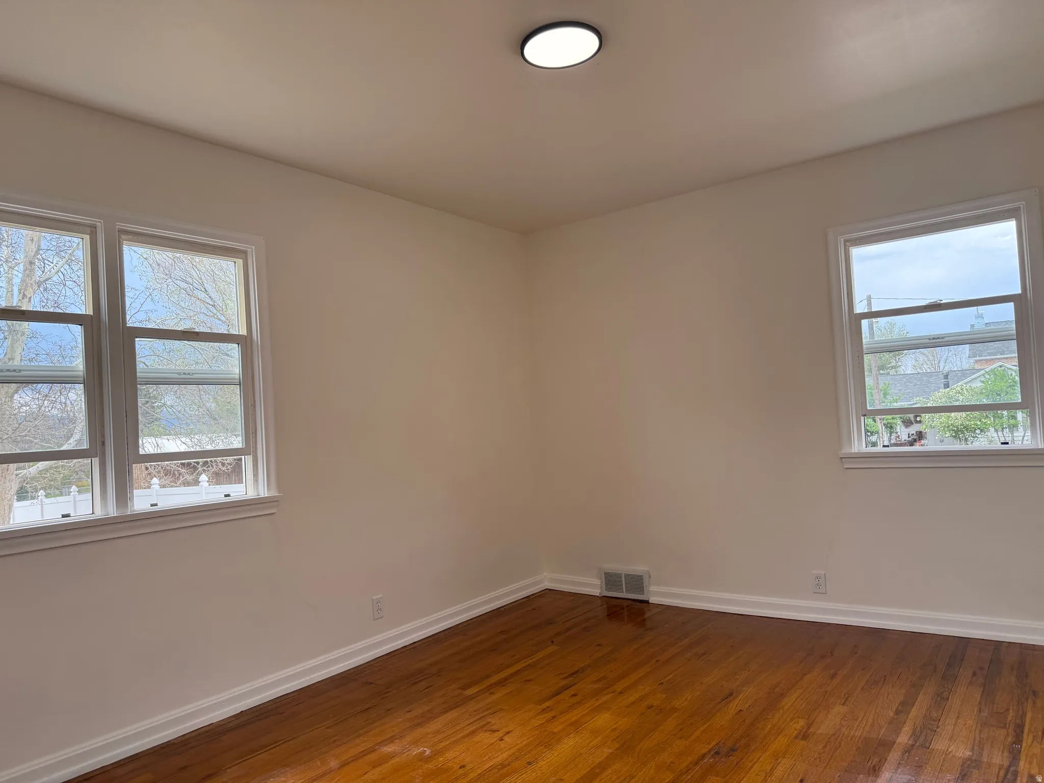 Room featuring wood flooring, white trim, two windows, and a flush-mount ceiling light