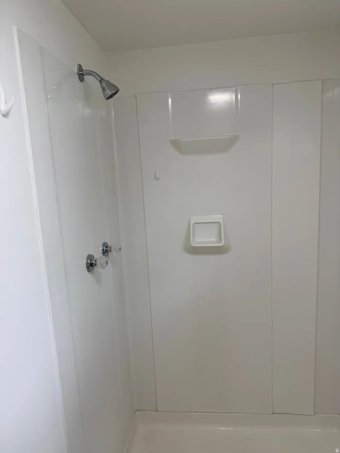 White shower enclosure with a chrome showerhead, clear acrylic faucet handles, and integrated shelving