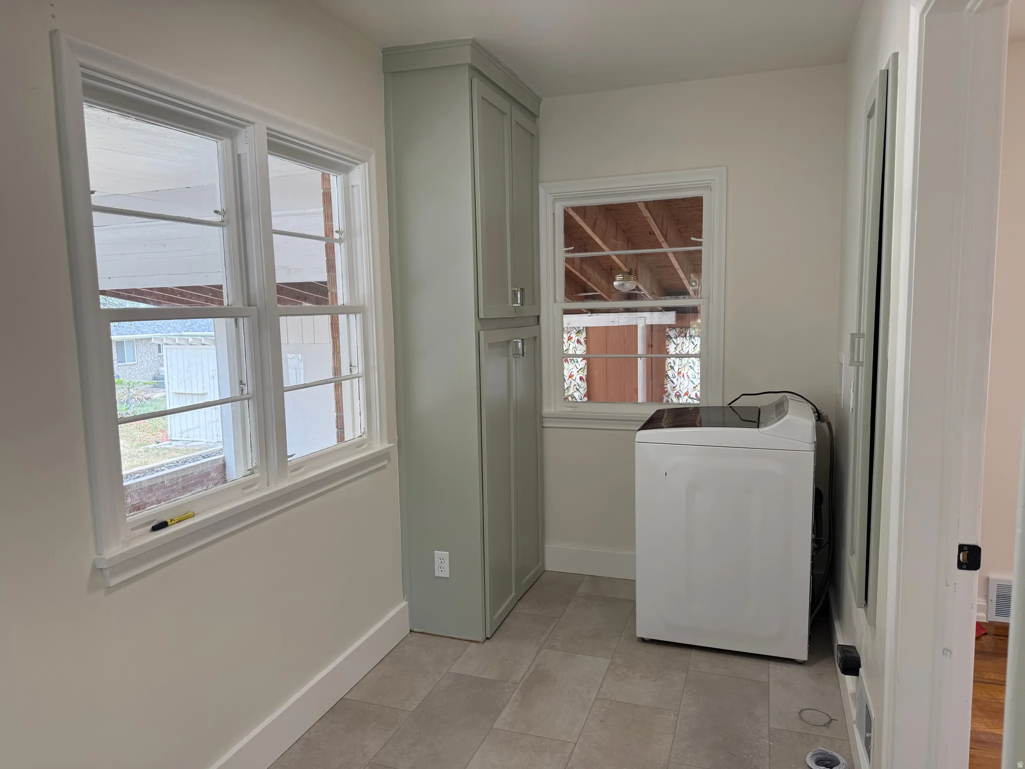 Laundry area featuring tile flooring, a custom built-in cabinet with upper and lower storage, dual pane windows, and a separate single window with decorative glass