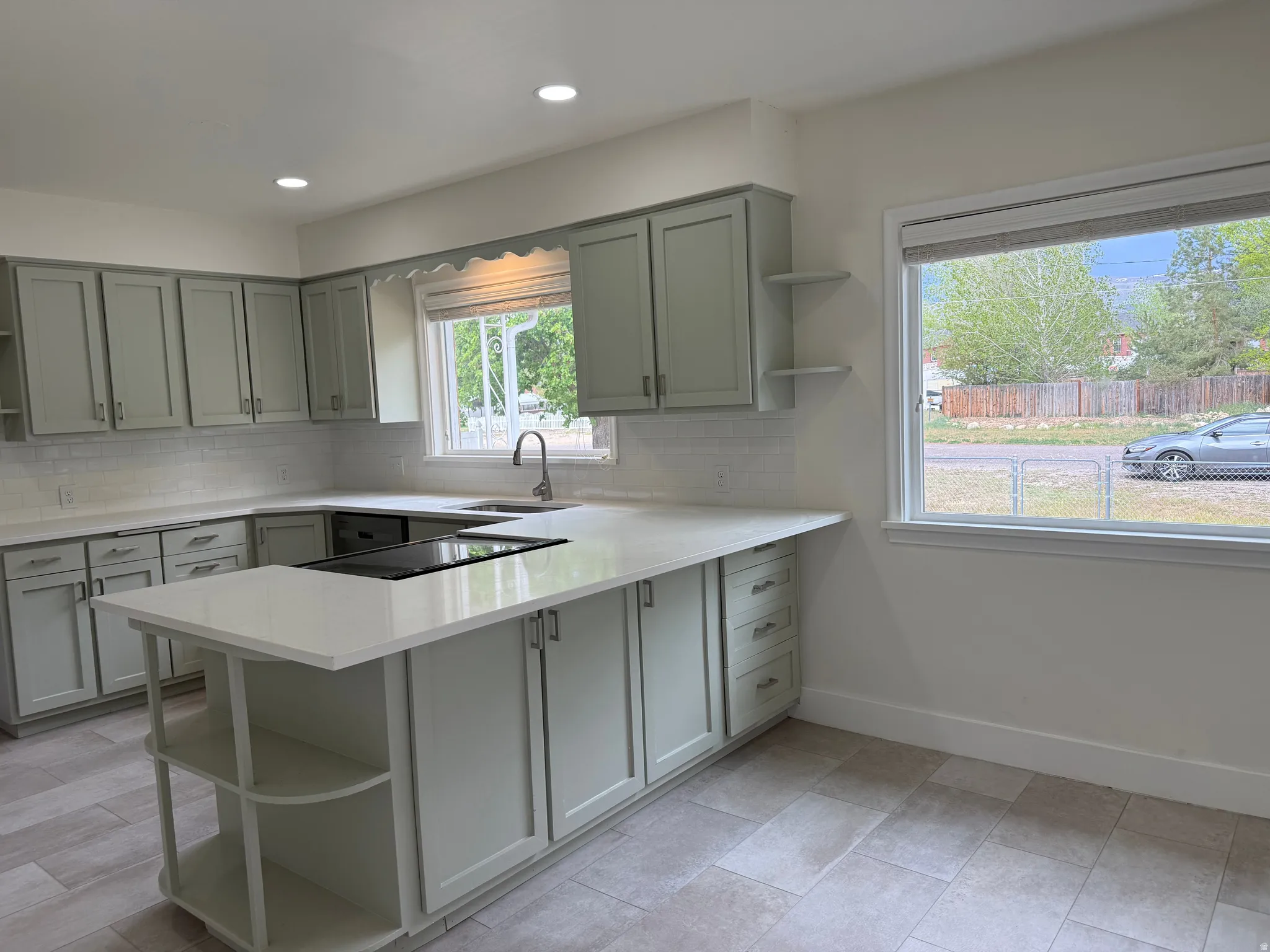 Kitchen featuring light-toned cabinetry, white countertops, subway tile backsplash, a large center island with built-in cooktop, and neutral tile flooring