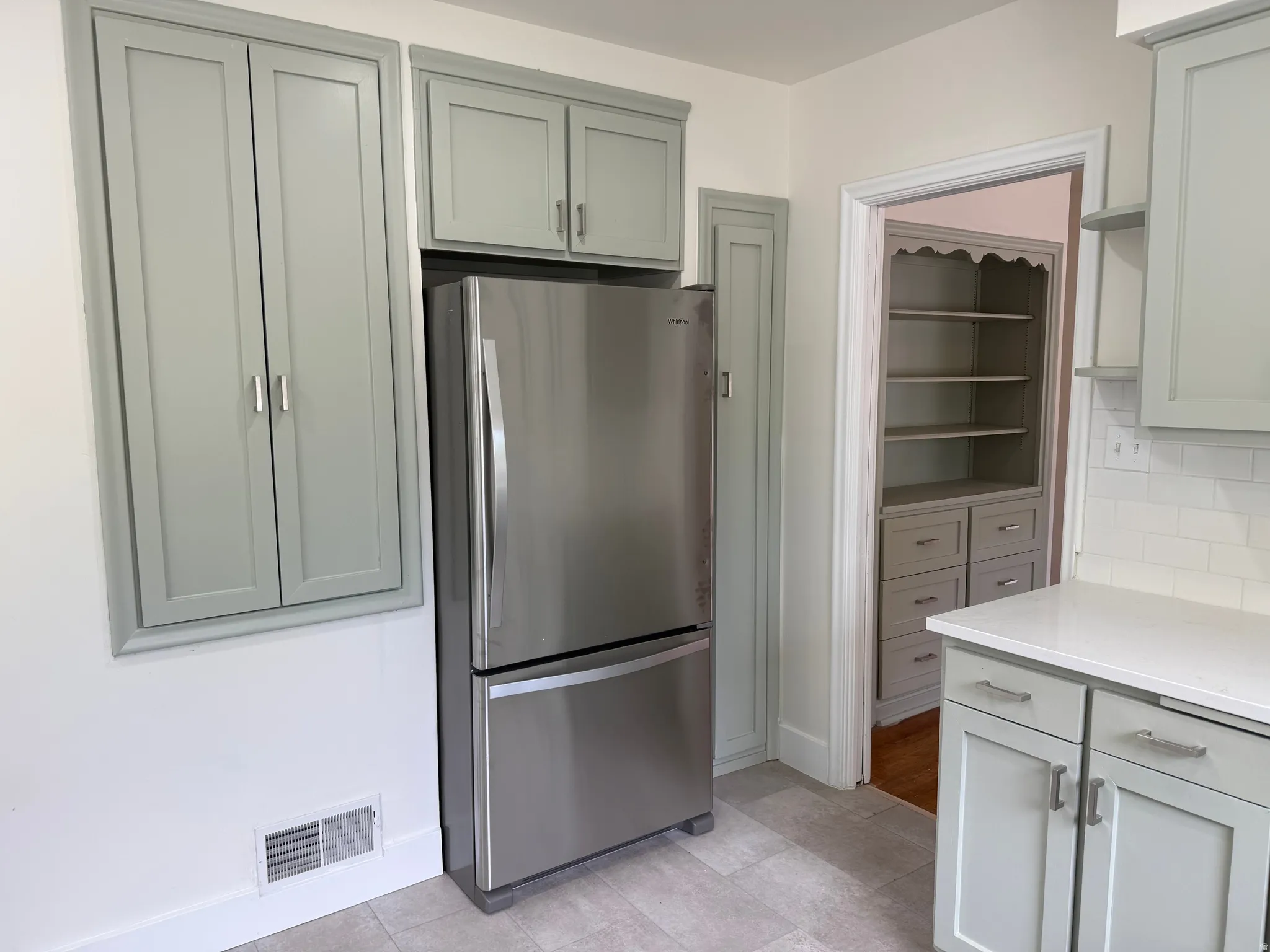 Kitchen featuring light gray cabinetry, stainless steel refrigerator, white subway tile backsplash, and light-colored countertops
