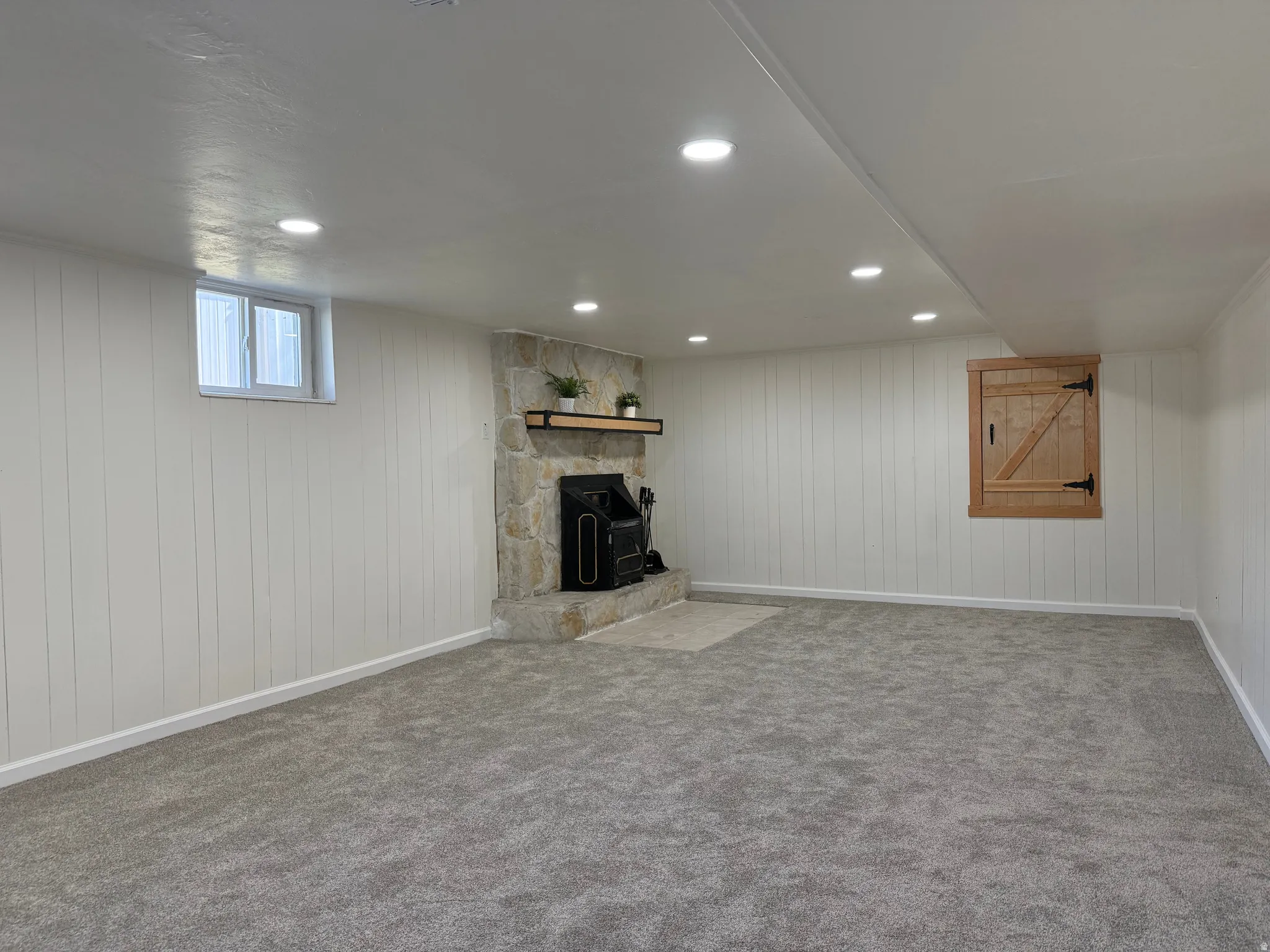 Spacious room featuring plush gray carpeting, white vertical plank walls, and recessed lighting