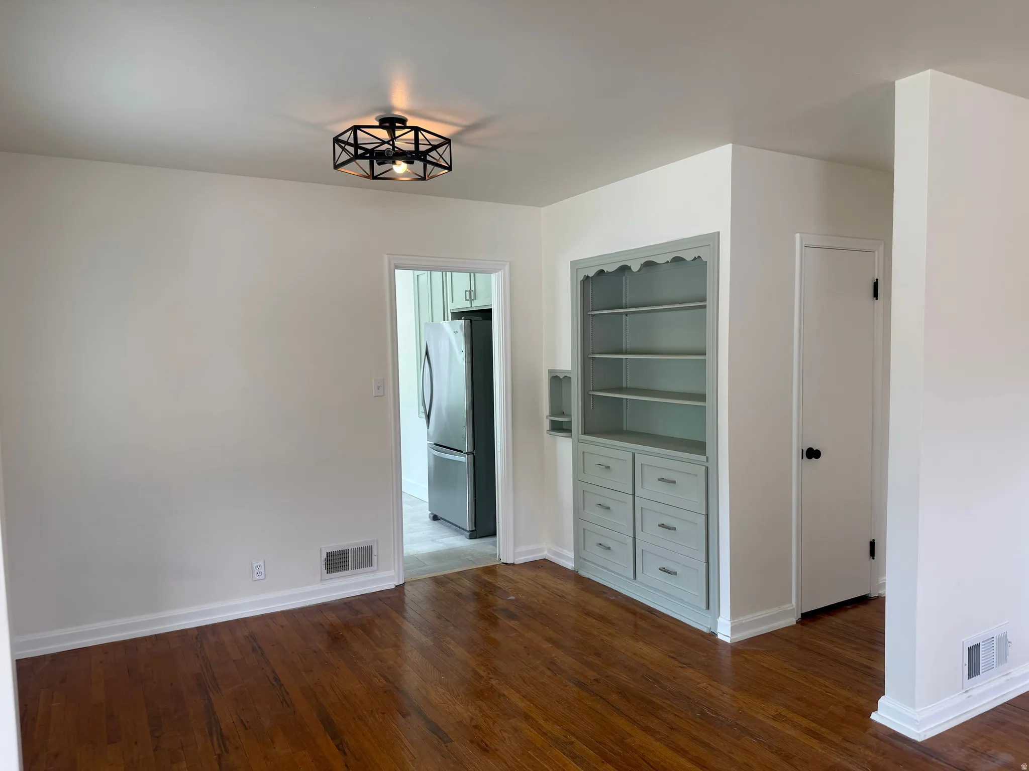 Built-in shelving unit with lower drawers, hardwood flooring, overhead semi-flush mount lighting, white baseboards, and a doorway opening