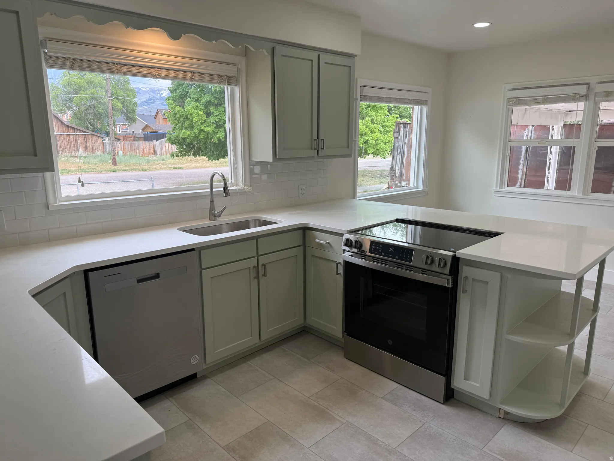 Kitchen featuring light-toned cabinetry, white countertops, tile flooring, stainless steel appliances, and multiple windows