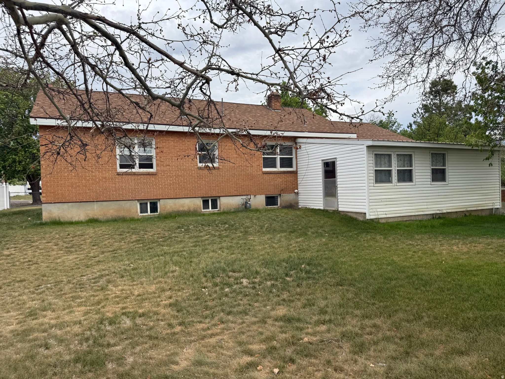 Brick and siding exterior featuring multiple windows and a brown shingle roof