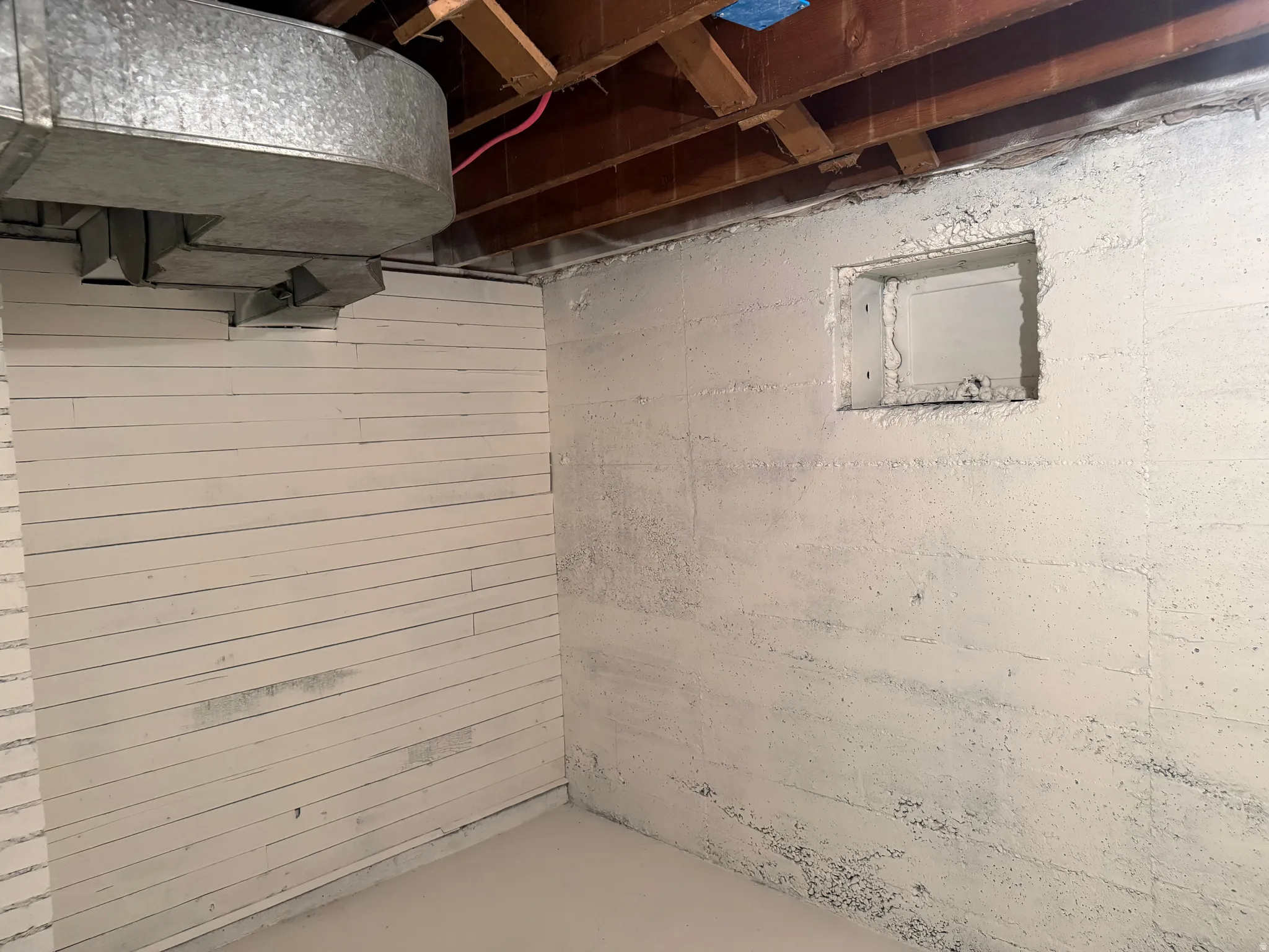 Unfinished basement space featuring exposed wood joists and a galvanized duct system