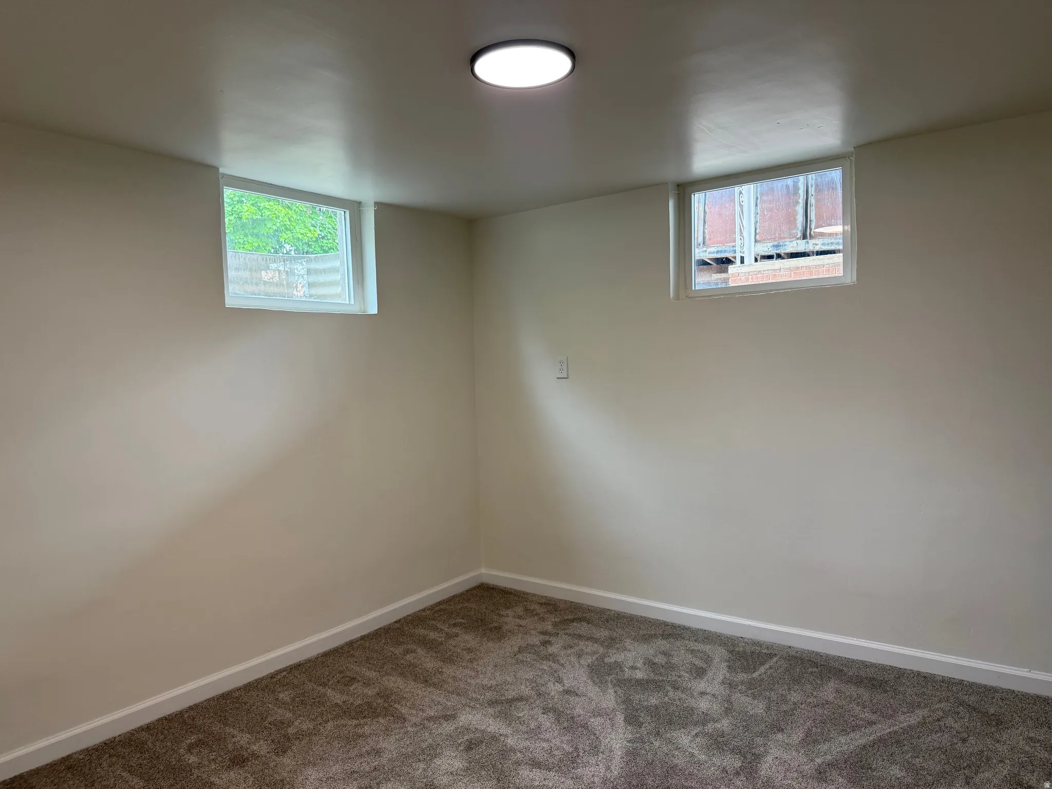 Neutral tone walls complementing new carpeting, featuring two perimeter windows and a flush-mount ceiling light