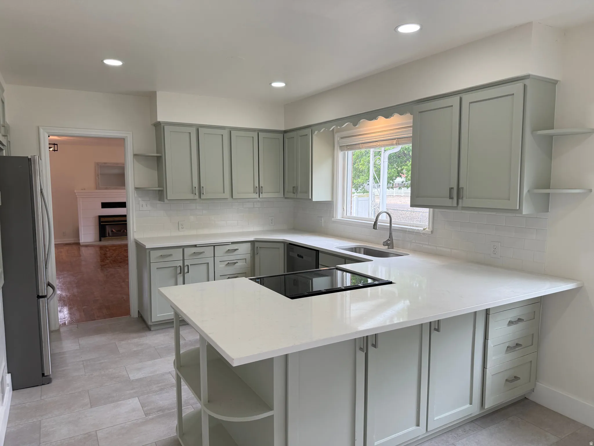 Modern kitchen featuring sage shaker cabinetry, white subway tile backsplash, and light-tone plank flooring