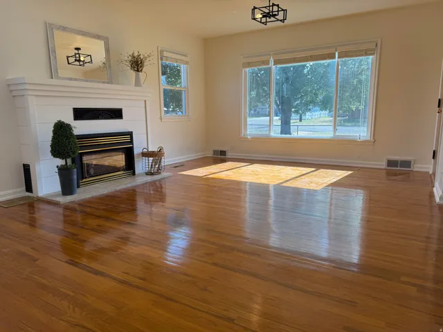 Spacious room featuring polished wood flooring, a fireplace with a white shiplap-style mantel, and a large picture window