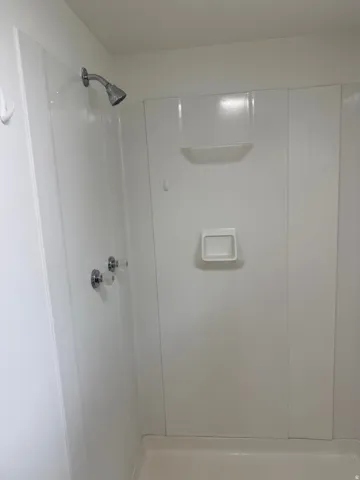 White shower enclosure with a chrome showerhead, clear acrylic faucet handles, and integrated shelving