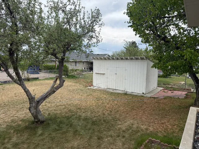 Expansive yard featuring a white storage shed with double doors, established trees, and a concrete pad