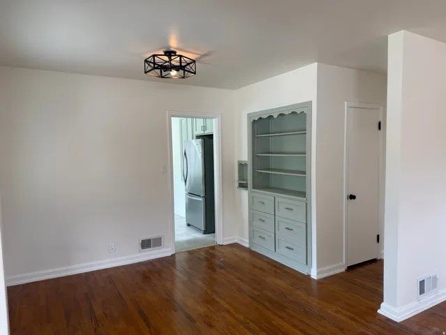 Built-in shelving unit with lower drawers, hardwood flooring, overhead semi-flush mount lighting, white baseboards, and a doorway opening