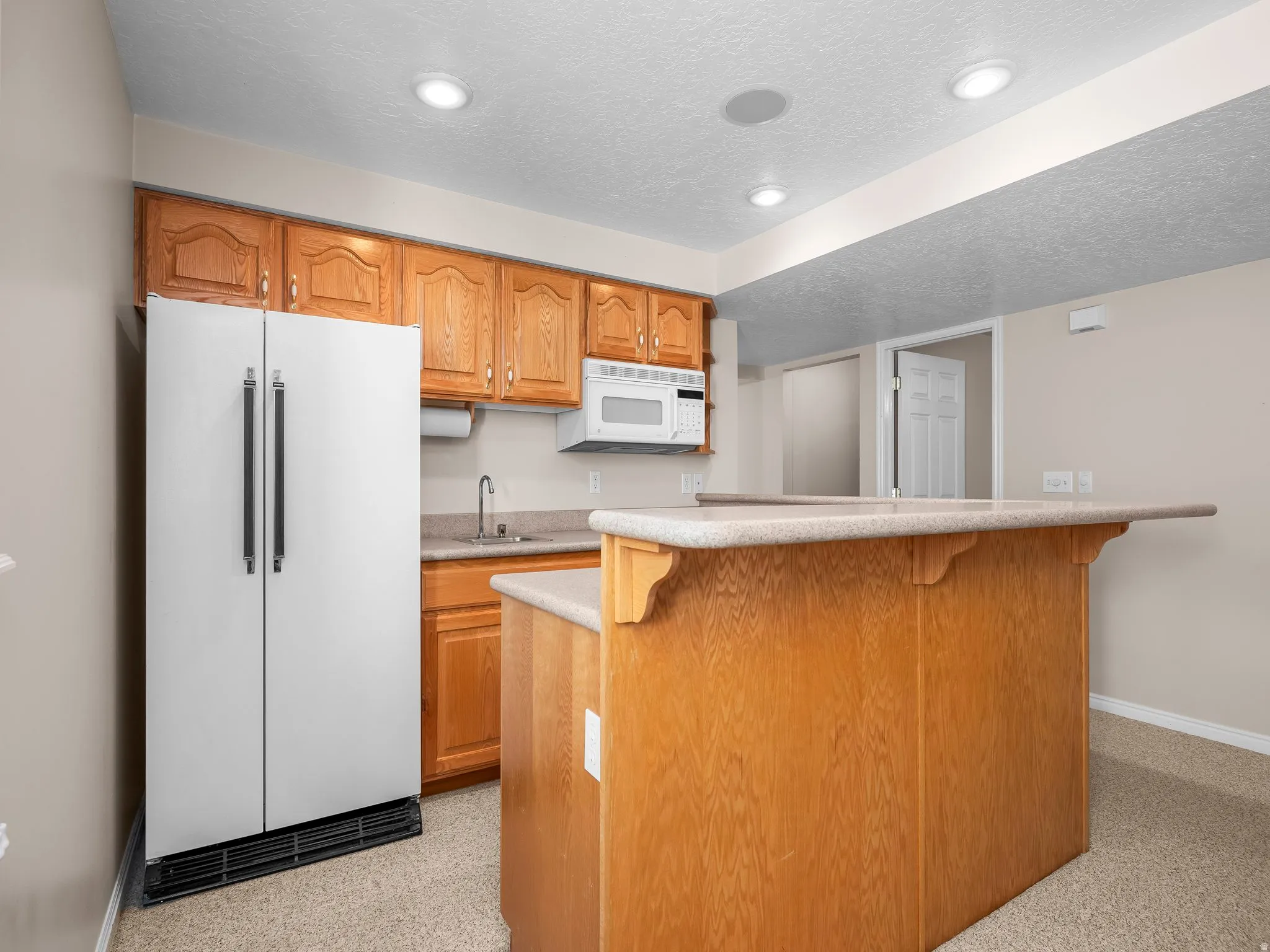 Kitchenette featuring a built-in microwave, wood cabinetry, a stainless steel sink, and a two-tier peninsula with an extended countertop
