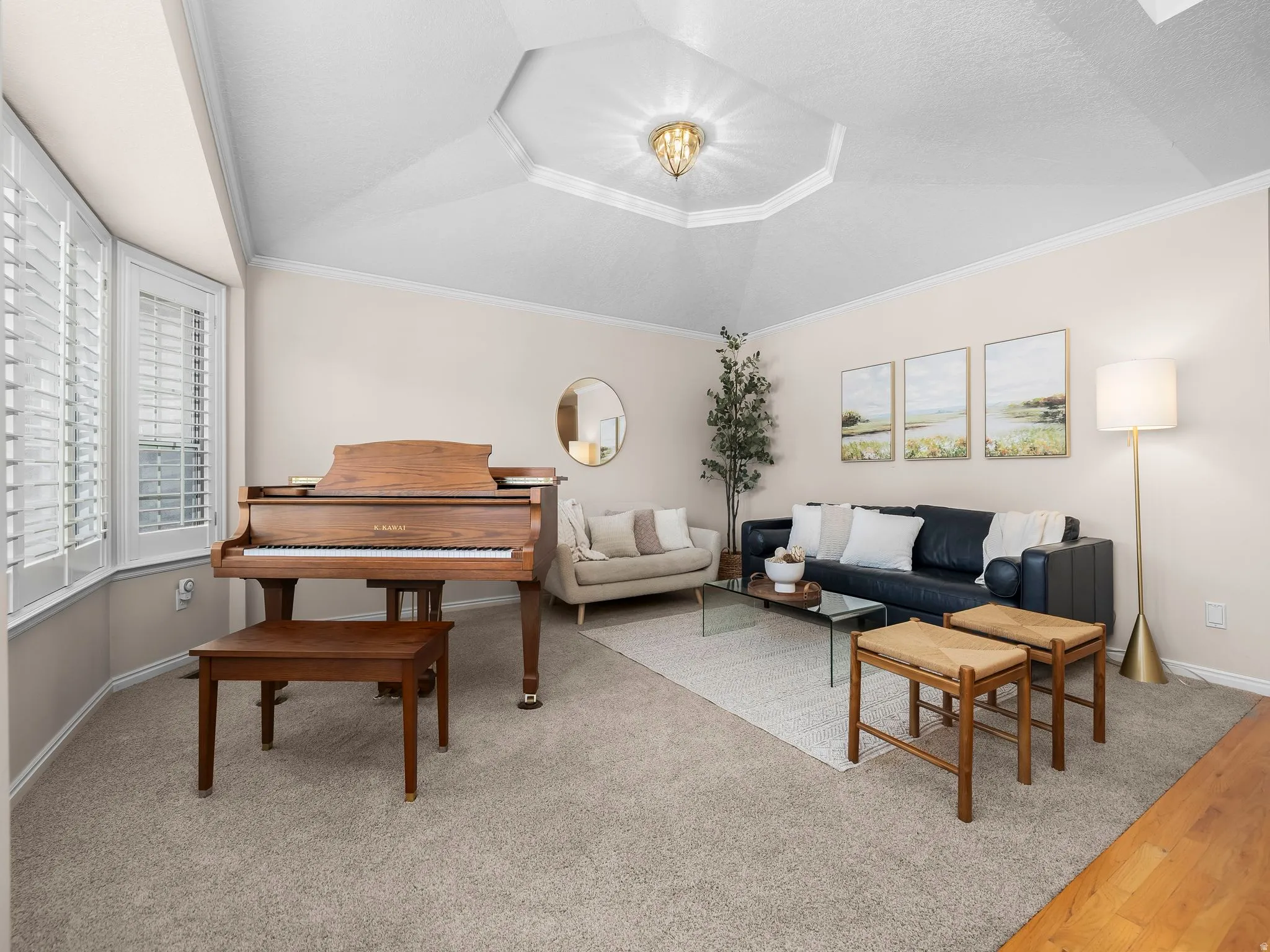 Carpeted living area featuring a bay window with plantation shutters, a multi-tiered tray ceiling with a central light fixture, and crown molding