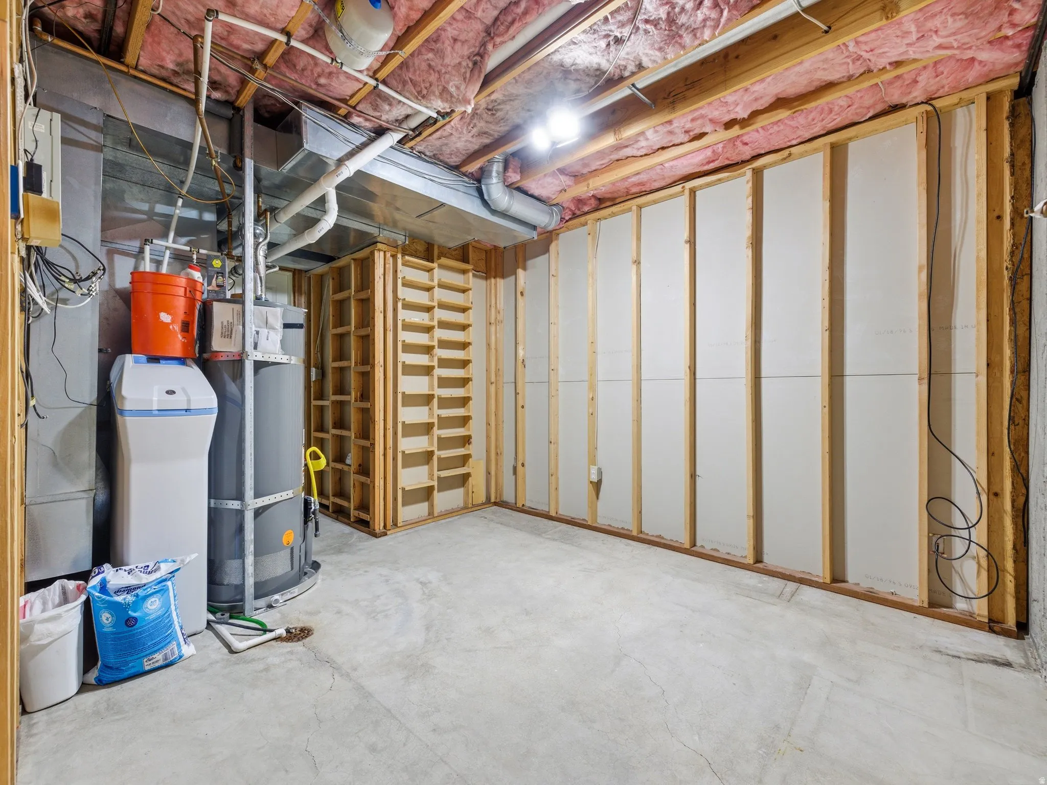 Unfinished basement space featuring exposed wood joists and insulation, a concrete floor, and framed walls