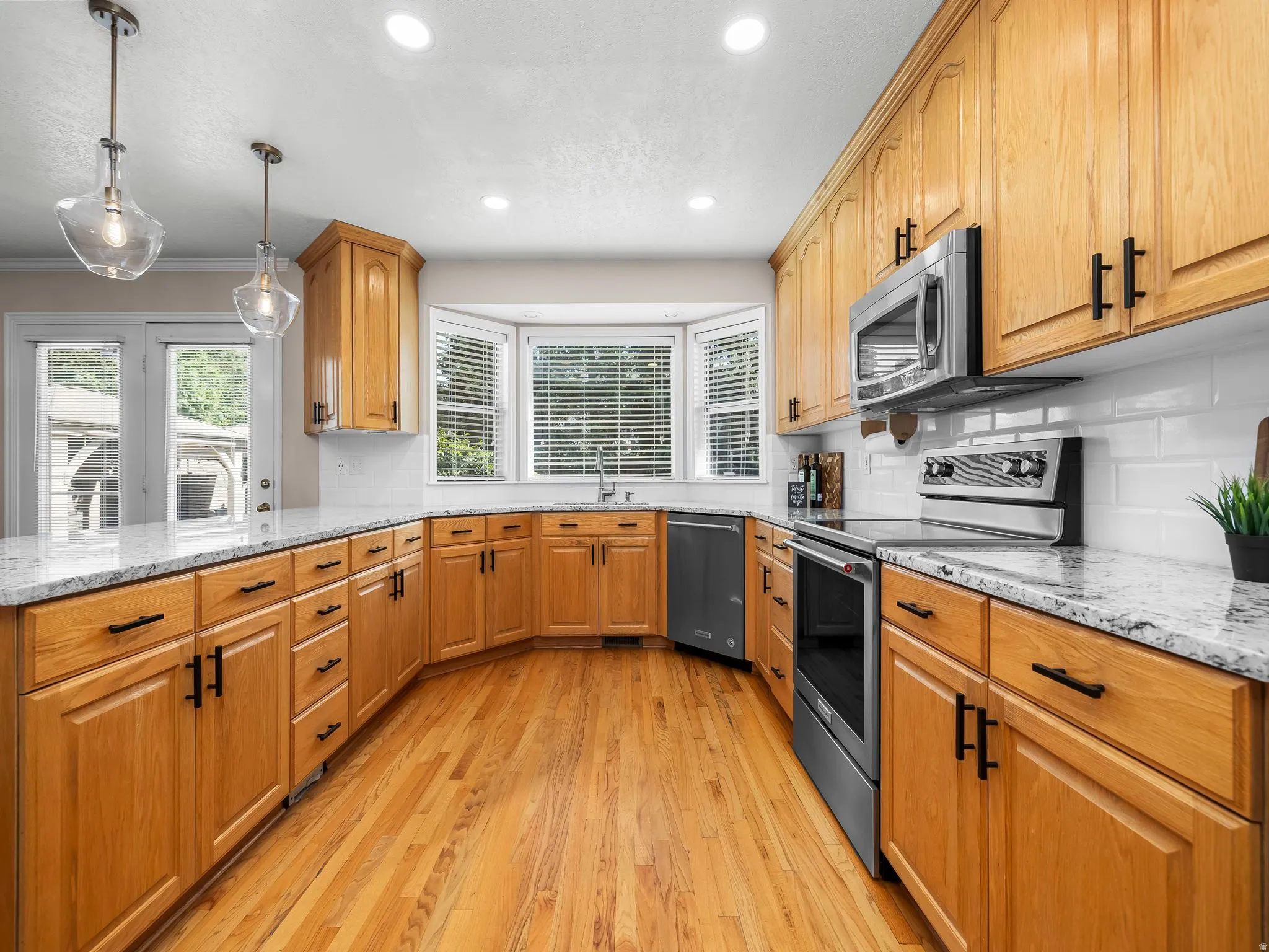Kitchen featuring light wood cabinetry with dark hardware, stainless steel appliances, granite-style countertops, white subway tile backsplash, and wood-finish flooring