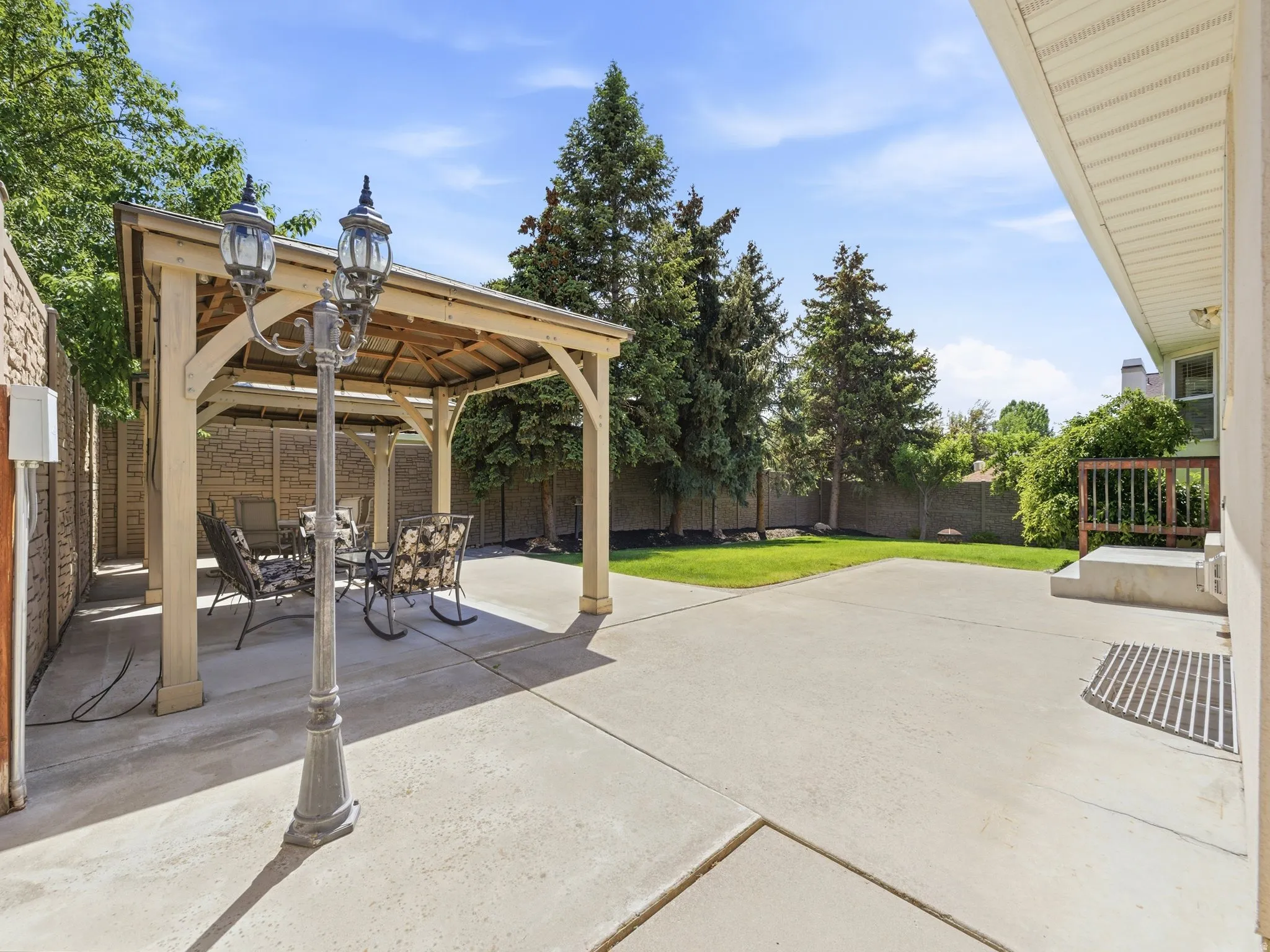Outdoor patio featuring a wooden pergola, concrete hardscaping, mature trees, and a manicured lawn