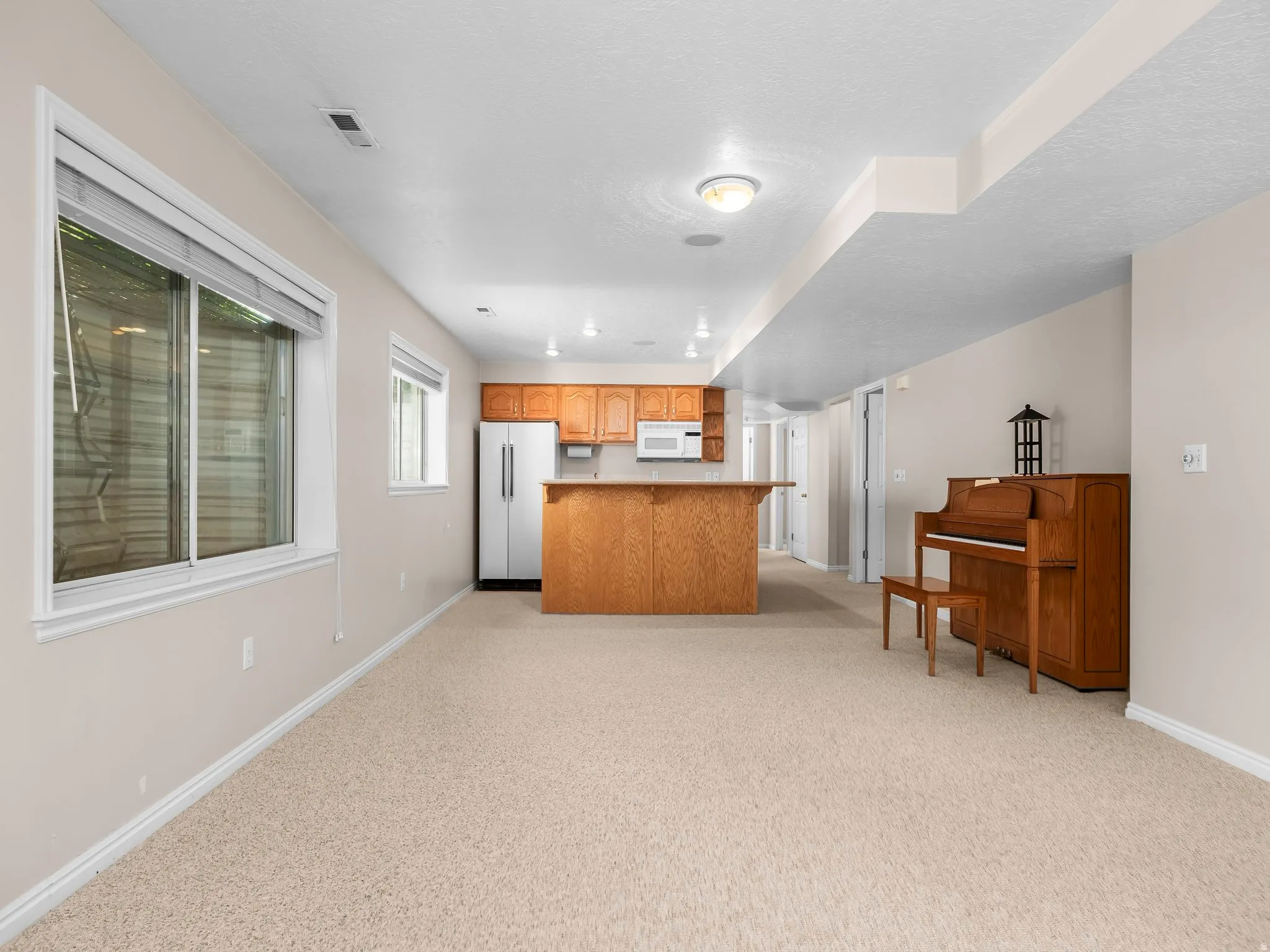Carpeted open-concept living area featuring a kitchen with light wood cabinetry and a peninsula breakfast bar
