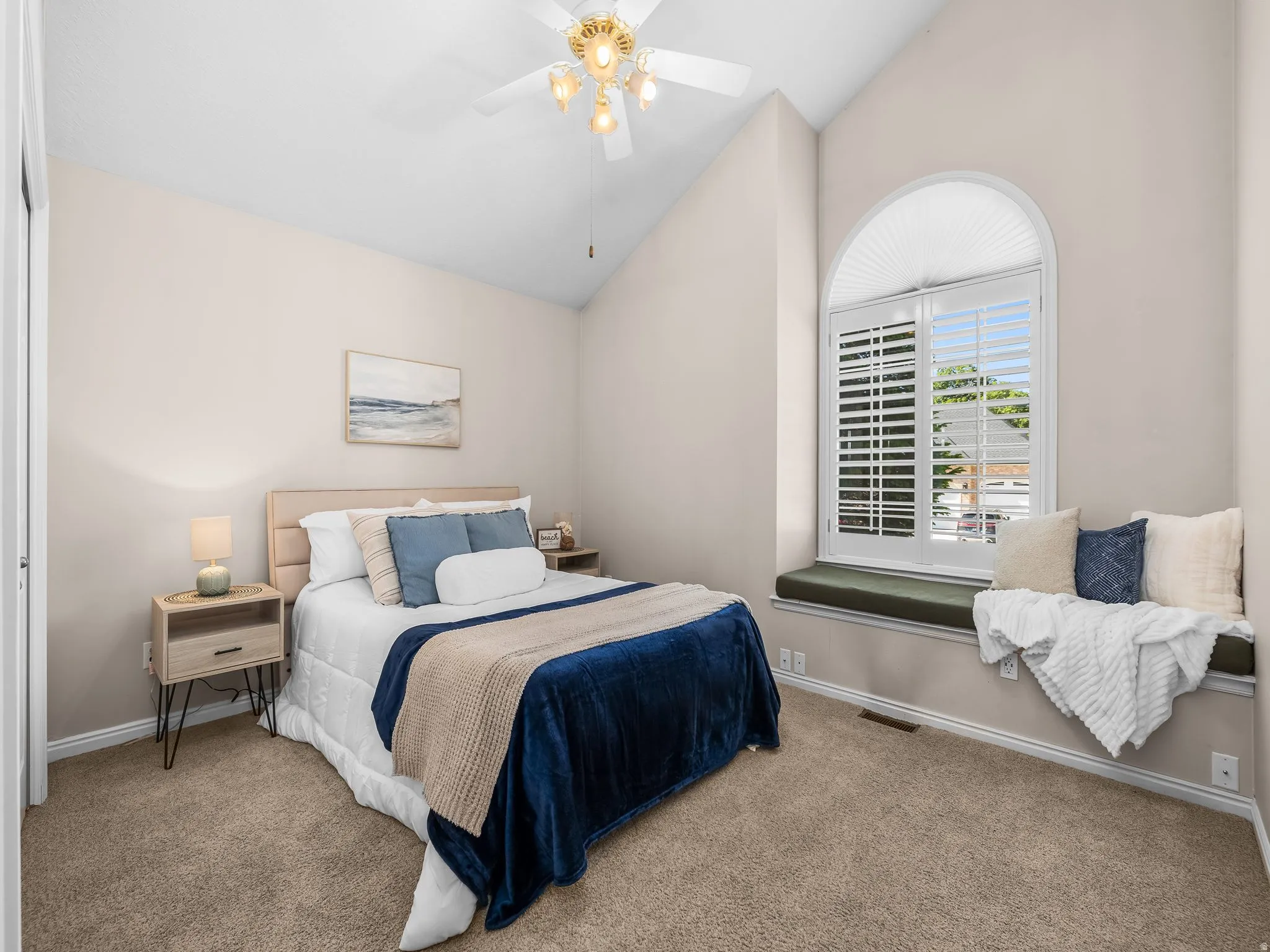 Room featuring a vaulted ceiling with a ceiling fan, arched window with plantation shutters and a cellular blind, and a built-in window seat