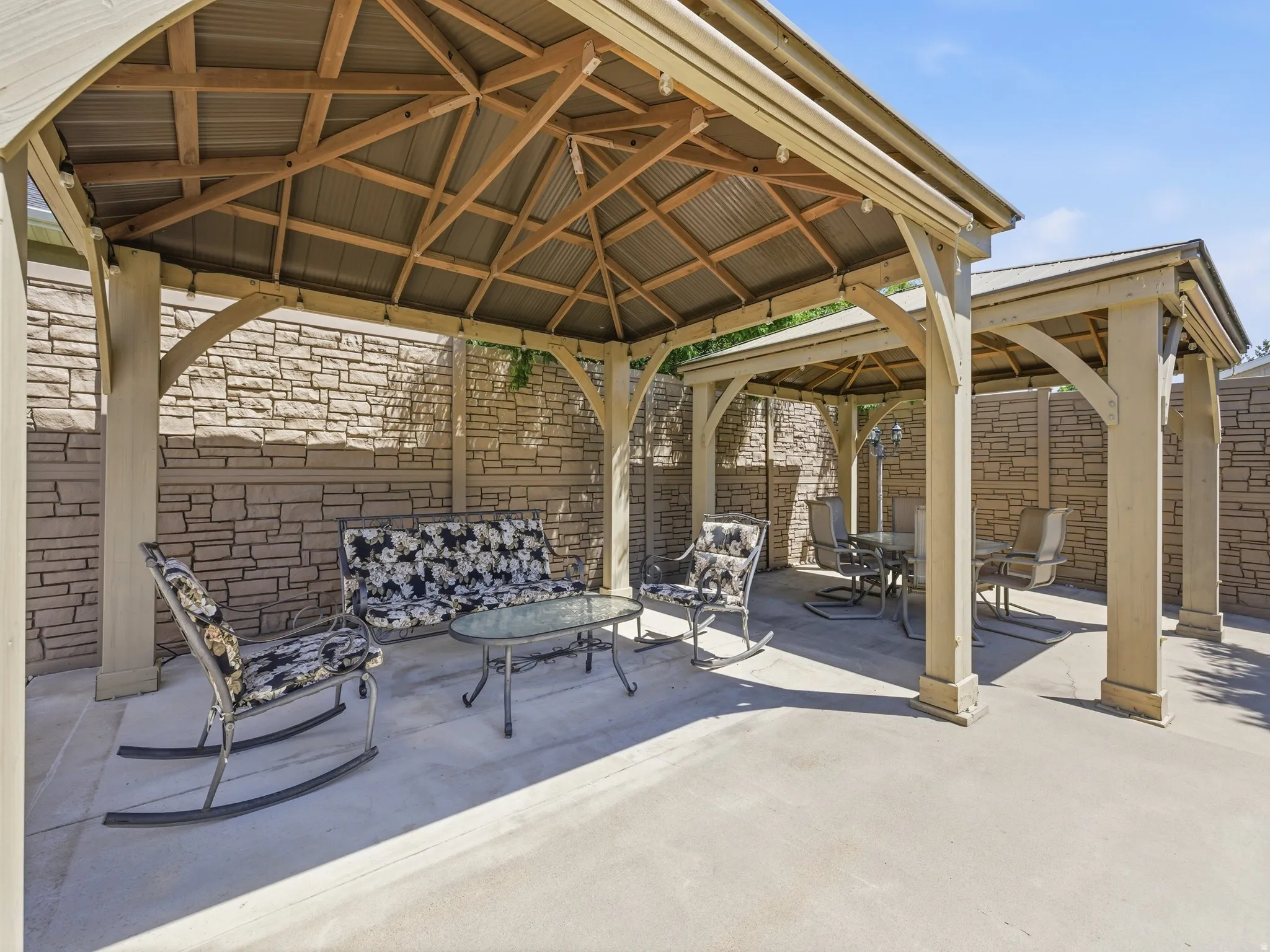 Expansive concrete patio featuring two connected pergolas with corrugated metal roofs and exposed wood framing