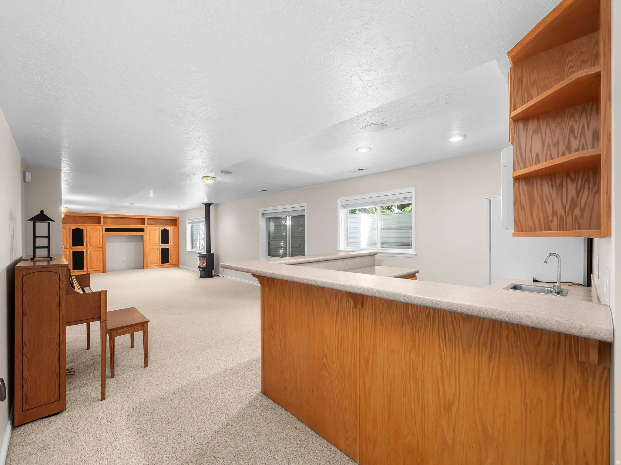 Open-concept room featuring a built-in wet bar with a sink, wood-finish cabinetry, and overhead shelving