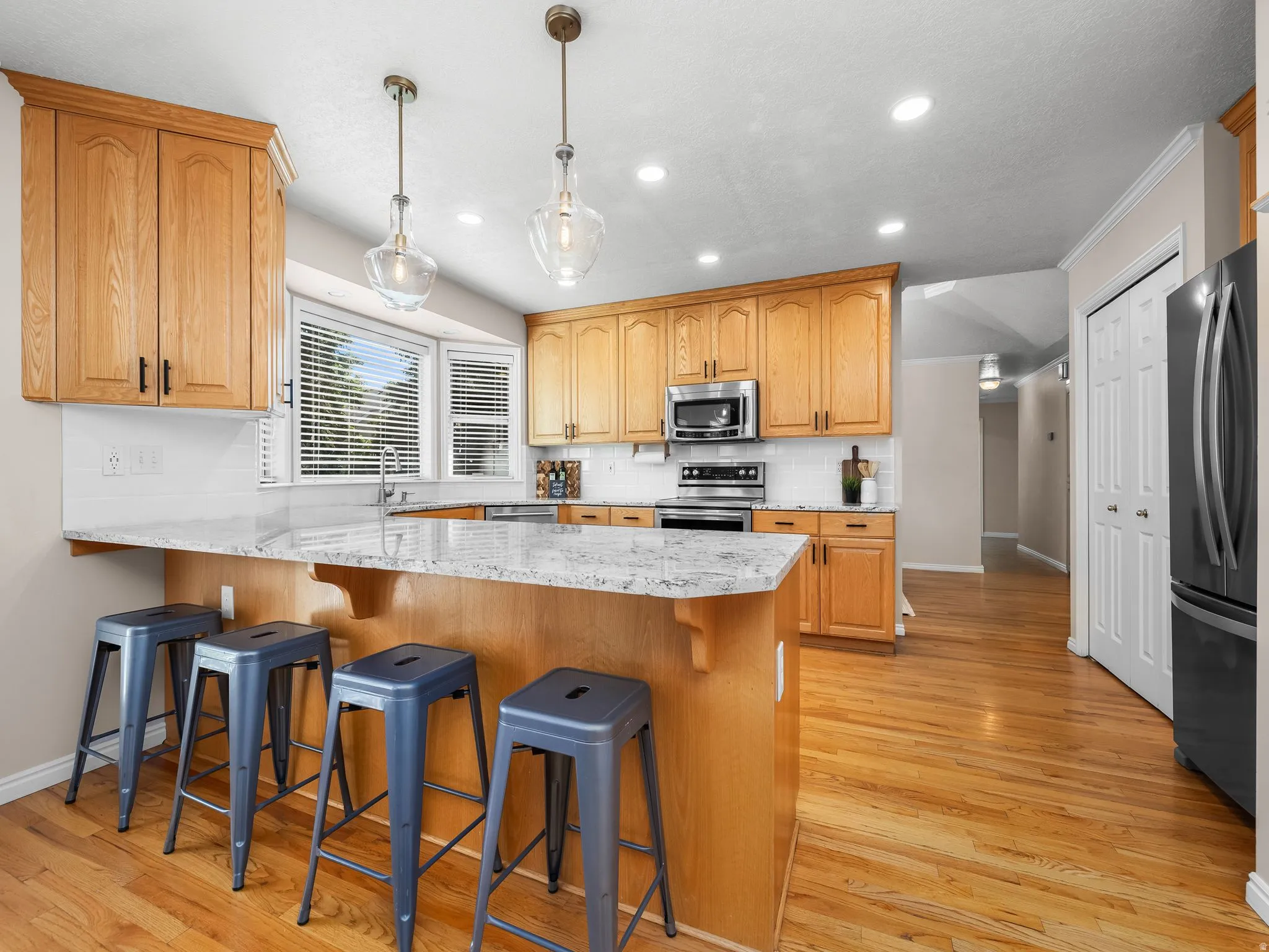 Kitchen featuring light wood cabinetry, white subway tile backsplash, stainless steel appliances, granite-style countertops, and wood-finish flooring