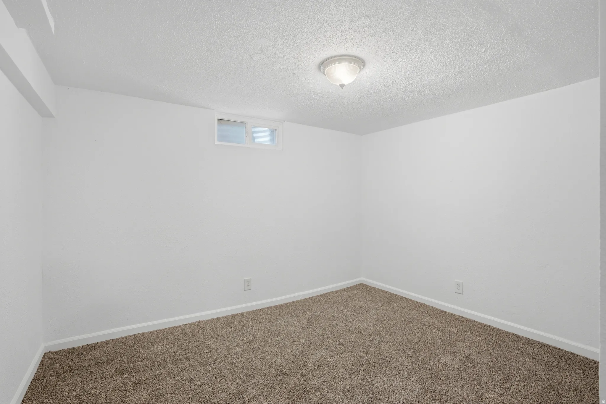 Neutral wall color, textured ceiling, flush mount ceiling light fixture, low-pile carpeting, and a high-set window