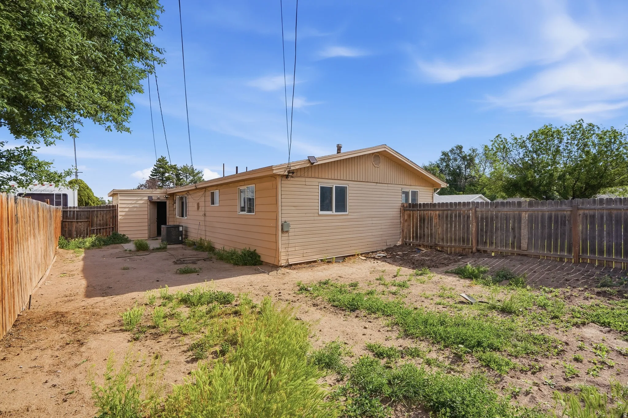 Expansive backyard featuring a fenced perimeter, tan siding, multiple windows, and mature trees