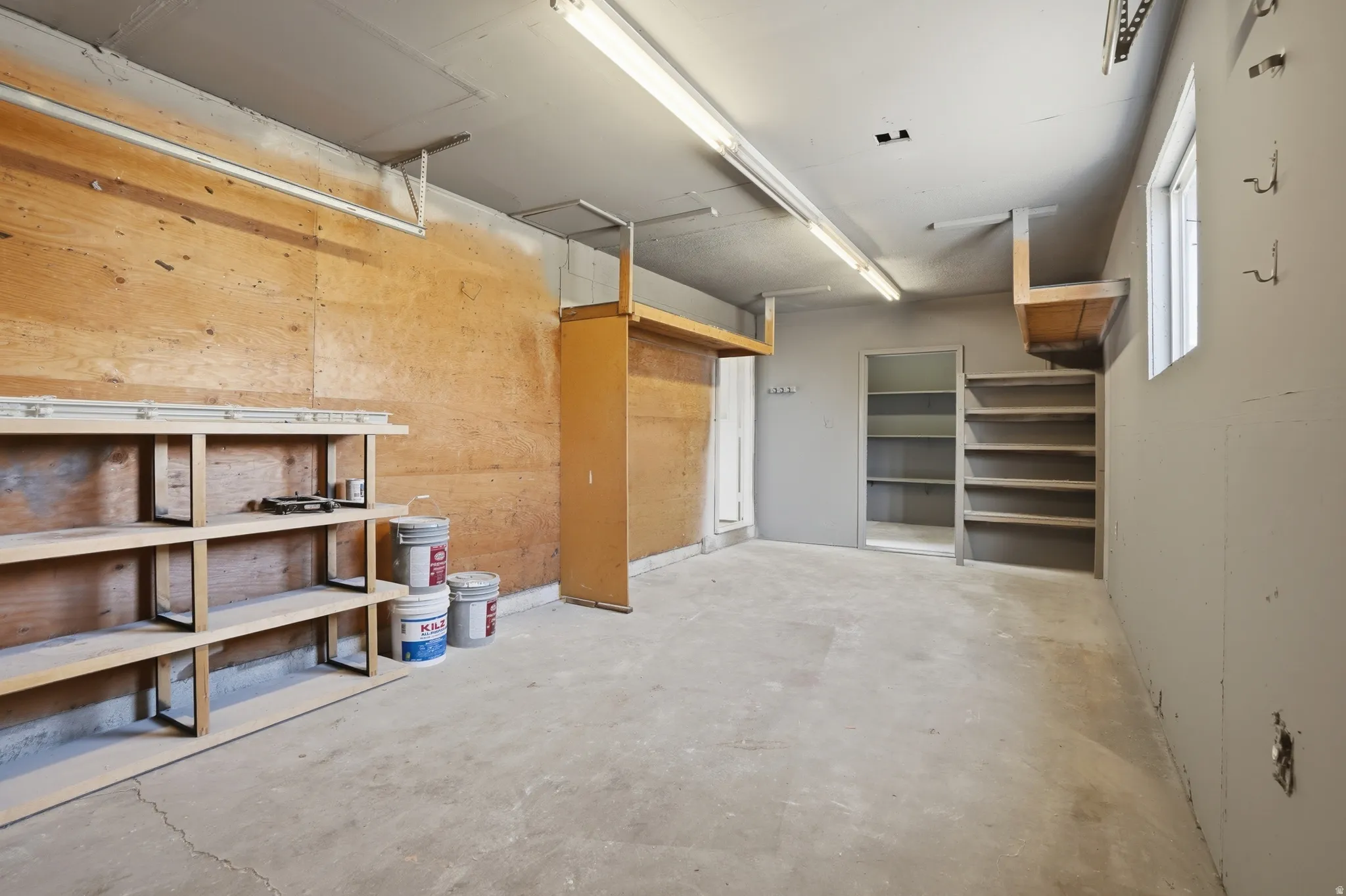 Spacious utility room featuring concrete flooring, built-in shelving, a window providing natural light, and overhead strip lighting