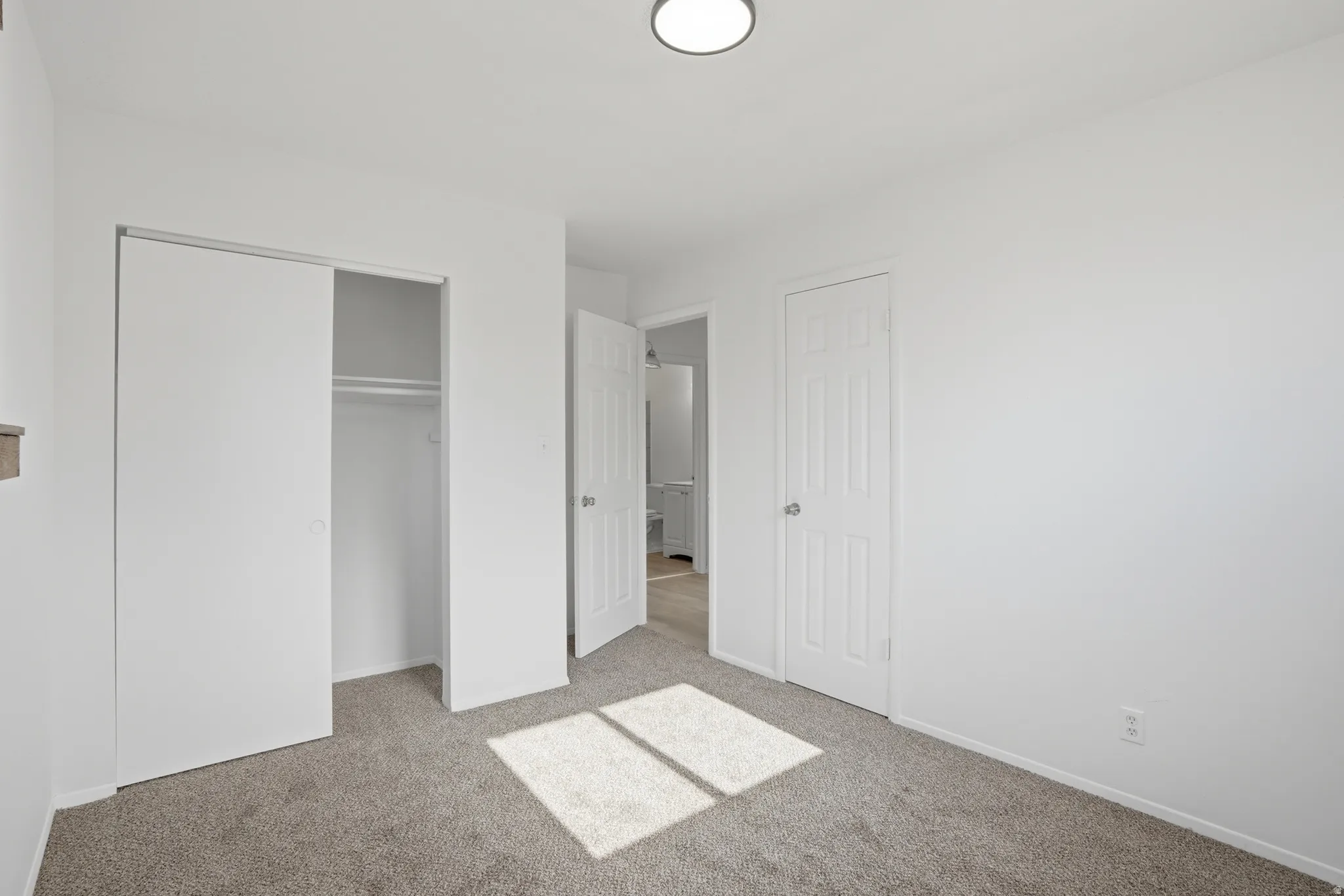 Bedroom featuring light gray carpeting, crisp white walls, a built-in closet with sliding doors, and a ceiling-mounted light fixture