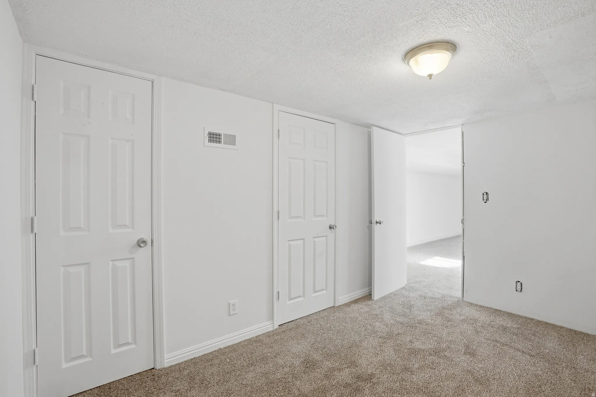 Neutral-toned carpeting extends throughout this room, featuring white walls and baseboards