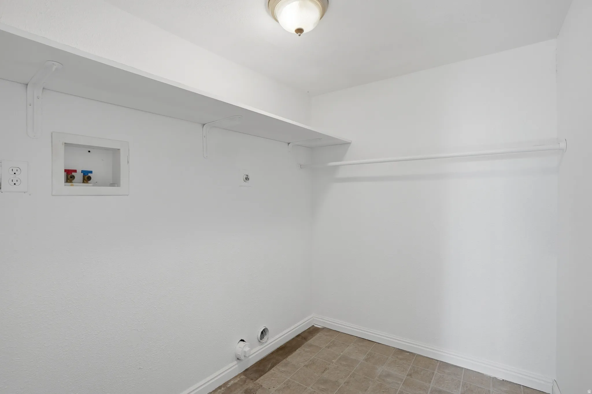 Laundry area featuring white walls, a built-in shelving unit, clothes rod, utility connections, and tile flooring