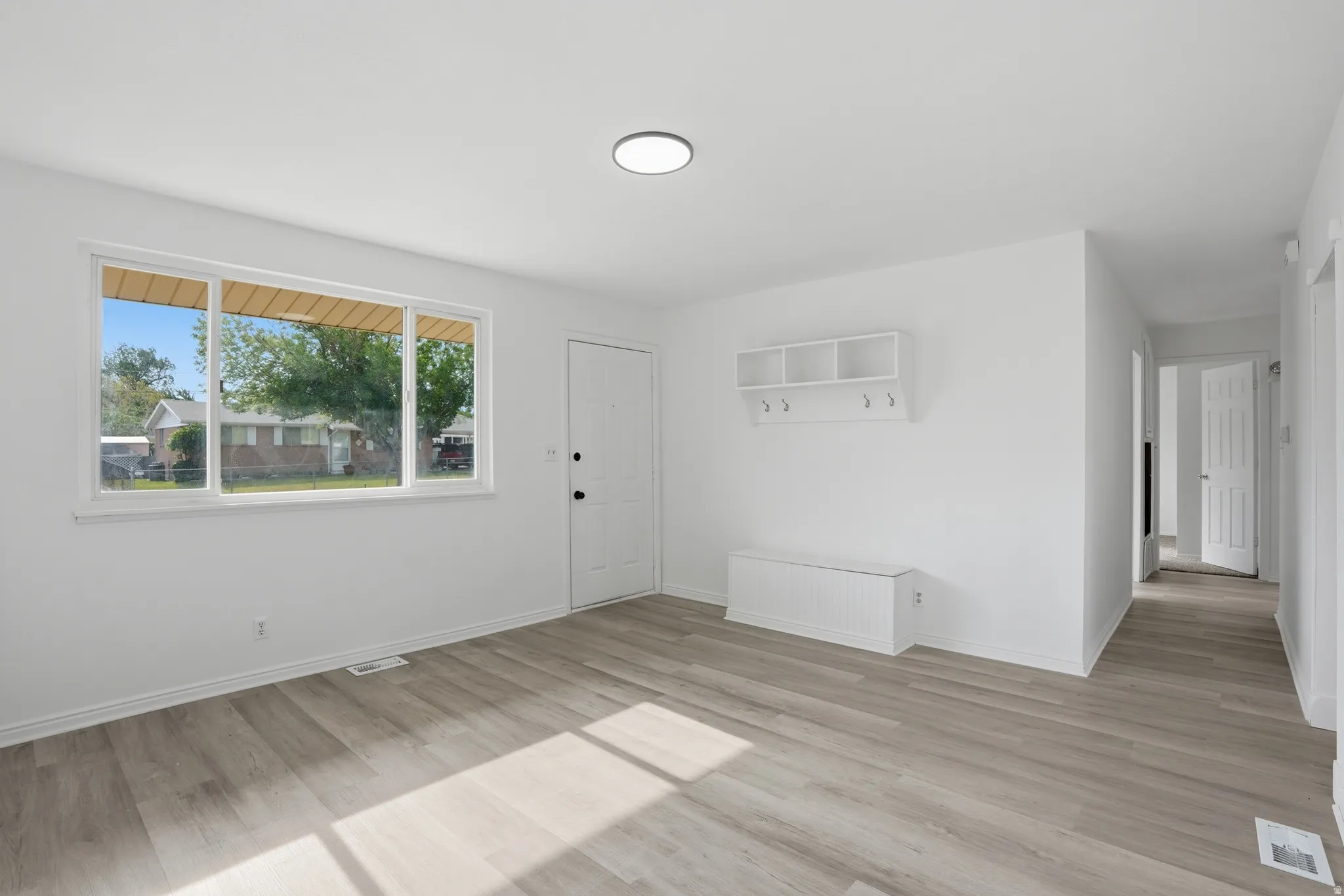 Bright main living space featuring plank wood-finish flooring, a contemporary ceiling light fixture, and a large multi-pane window