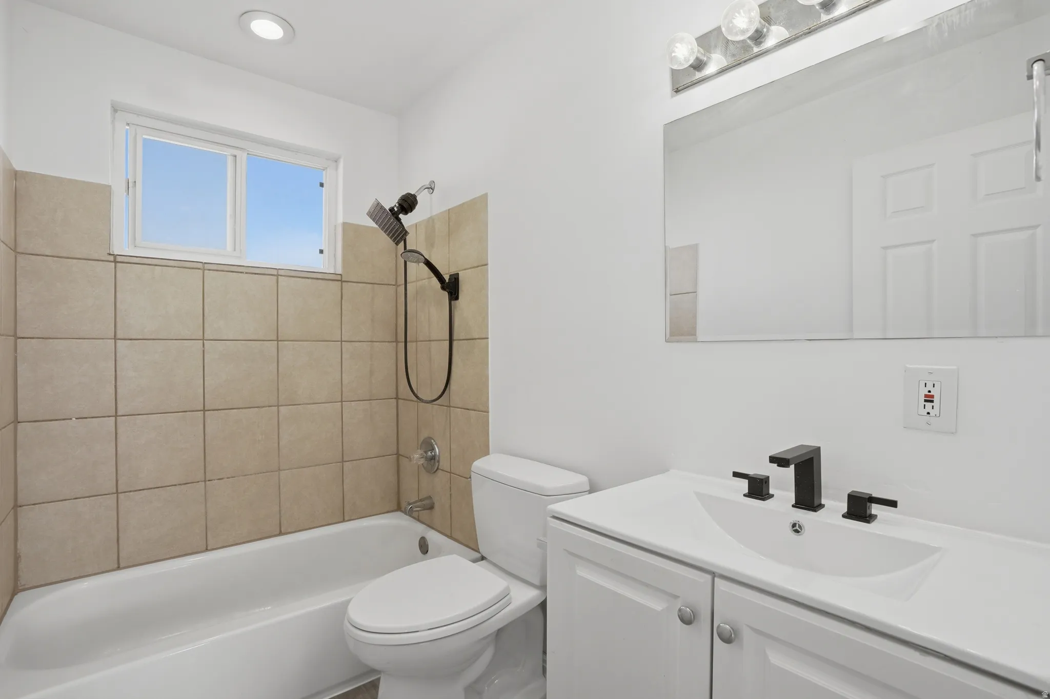 Bathroom featuring a white vanity with integrated sink, black fixtures, and a large wall mirror