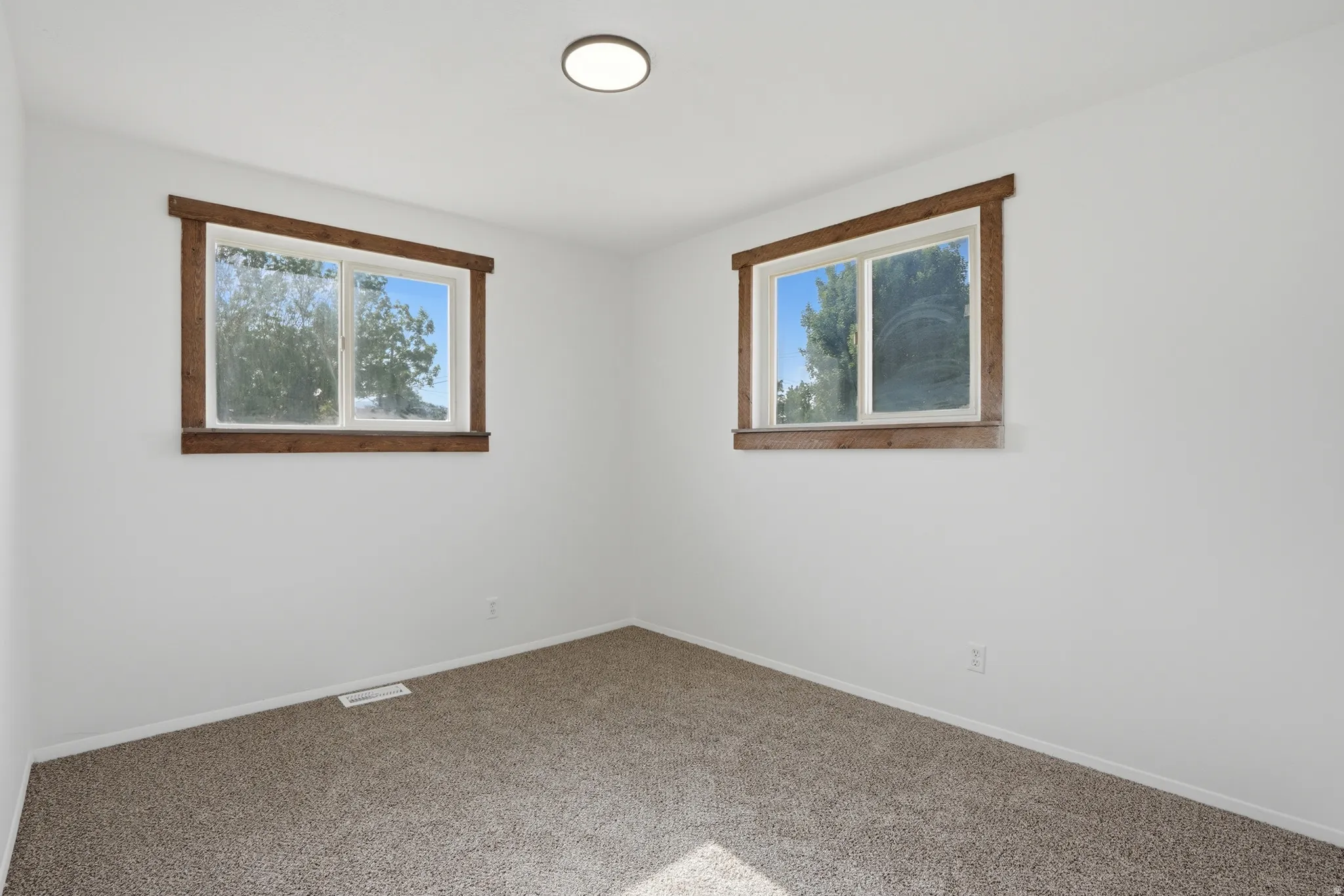 Neutral white walls featuring two windows with rustic wood-finish trim