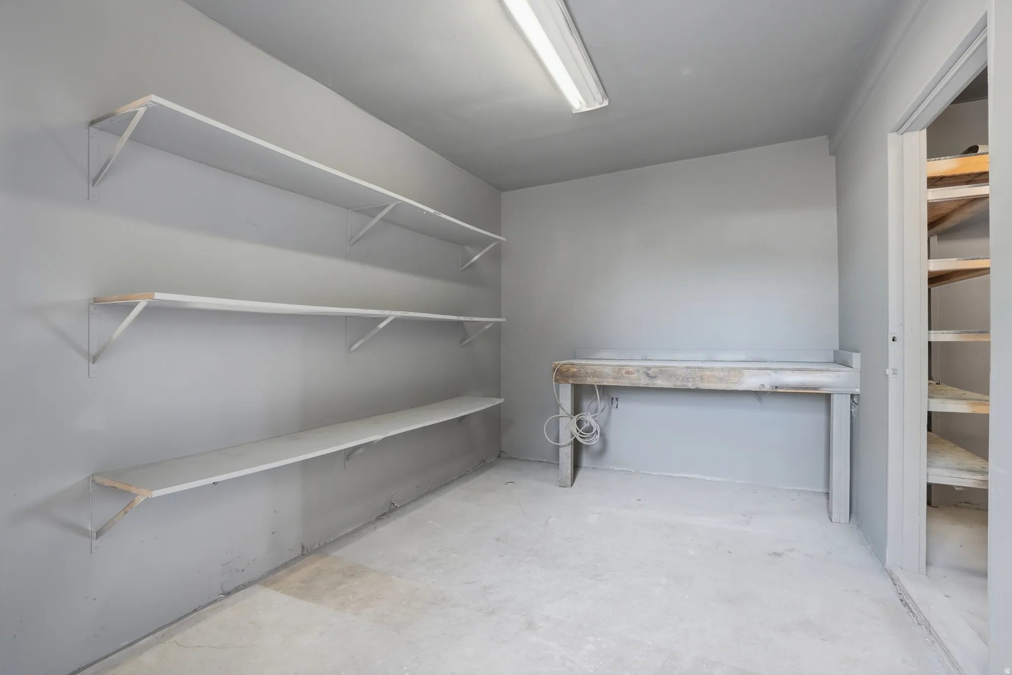Utility room featuring multiple shelving units, a built-in work surface, and concrete flooring