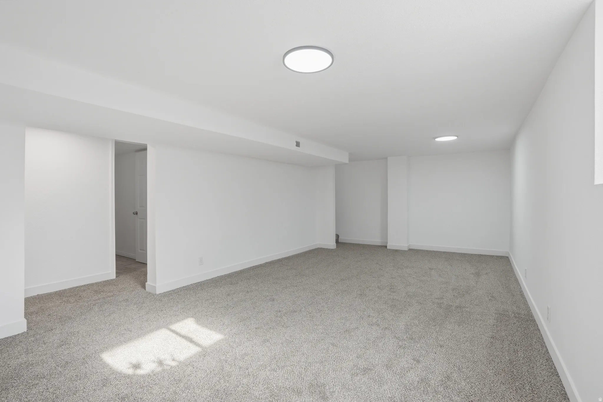 Spacious room featuring light gray carpet flooring and white painted walls