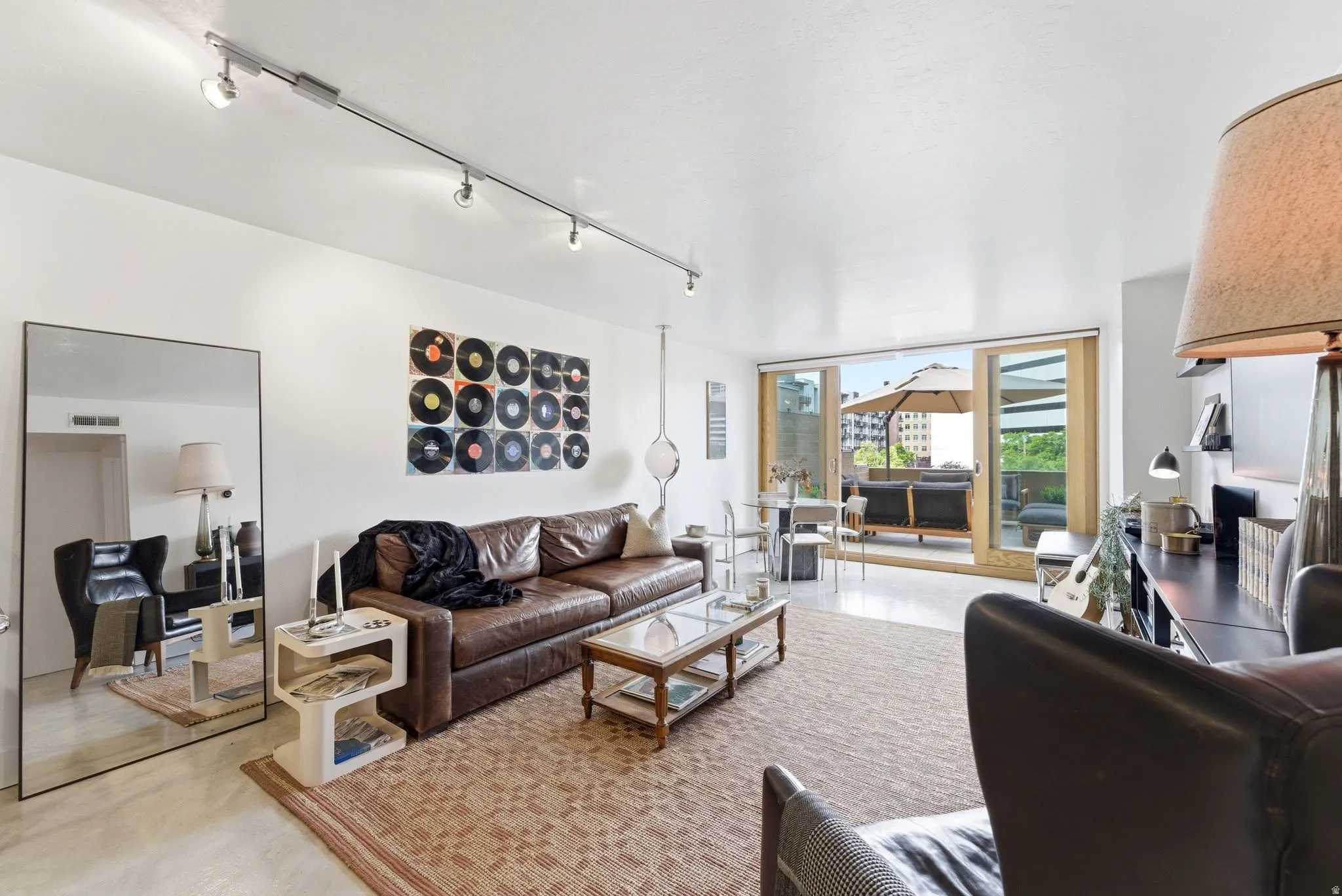 Living area featuring track lighting, light-toned flooring, and direct access to an outdoor patio with a visible umbrella