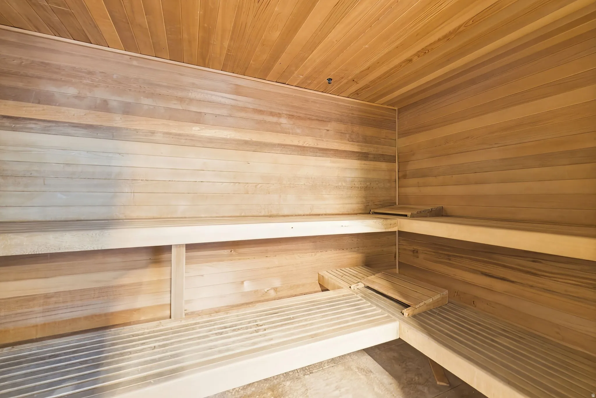 Sauna room featuring cedar plank walls and ceiling, multi-tiered wooden benches, and slatted wooden floor sections