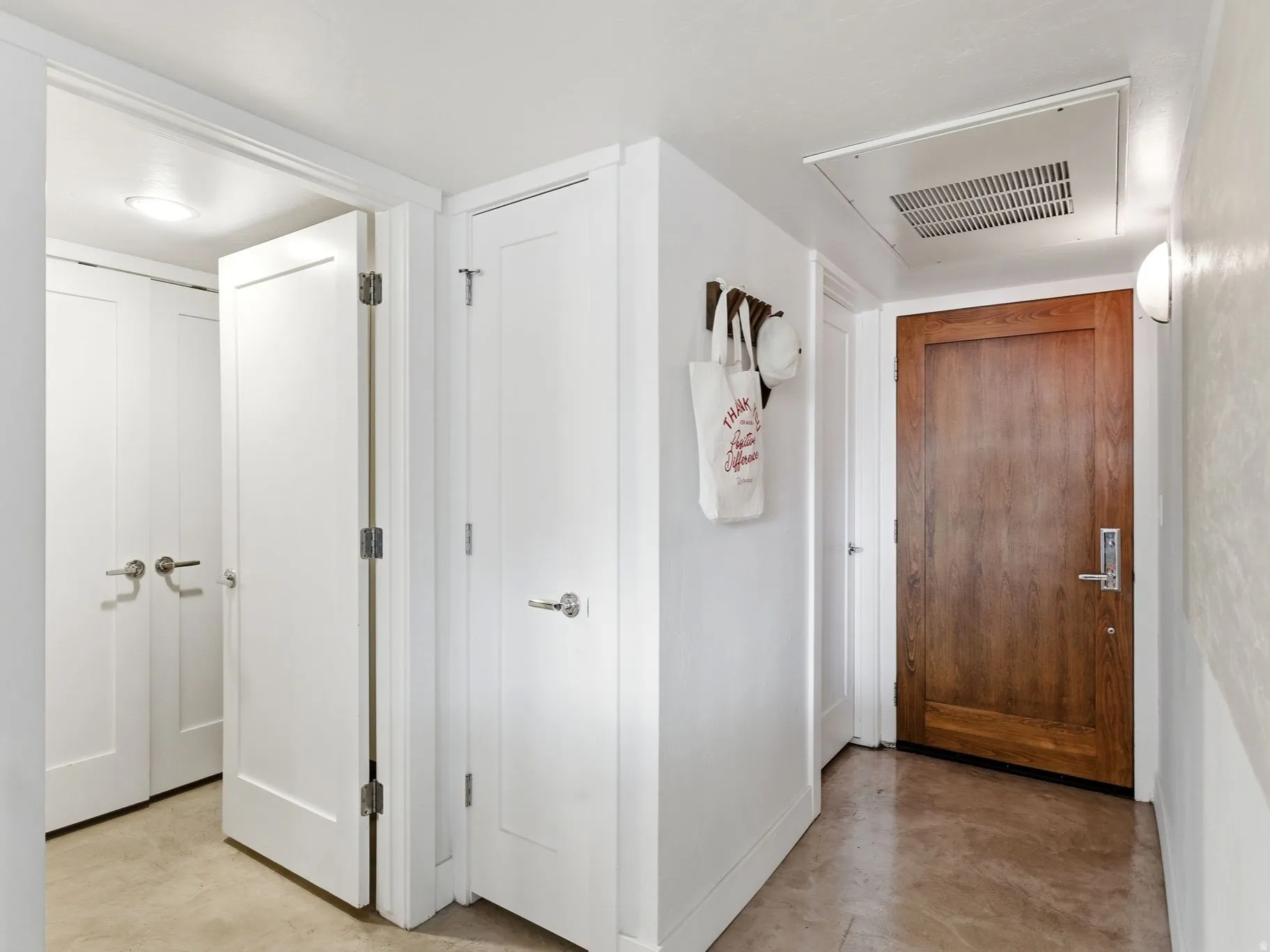 Hallway featuring a natural wood-finish door with brushed nickel hardware, bright white interior doors, recessed lighting, and a wall-mounted light fixture