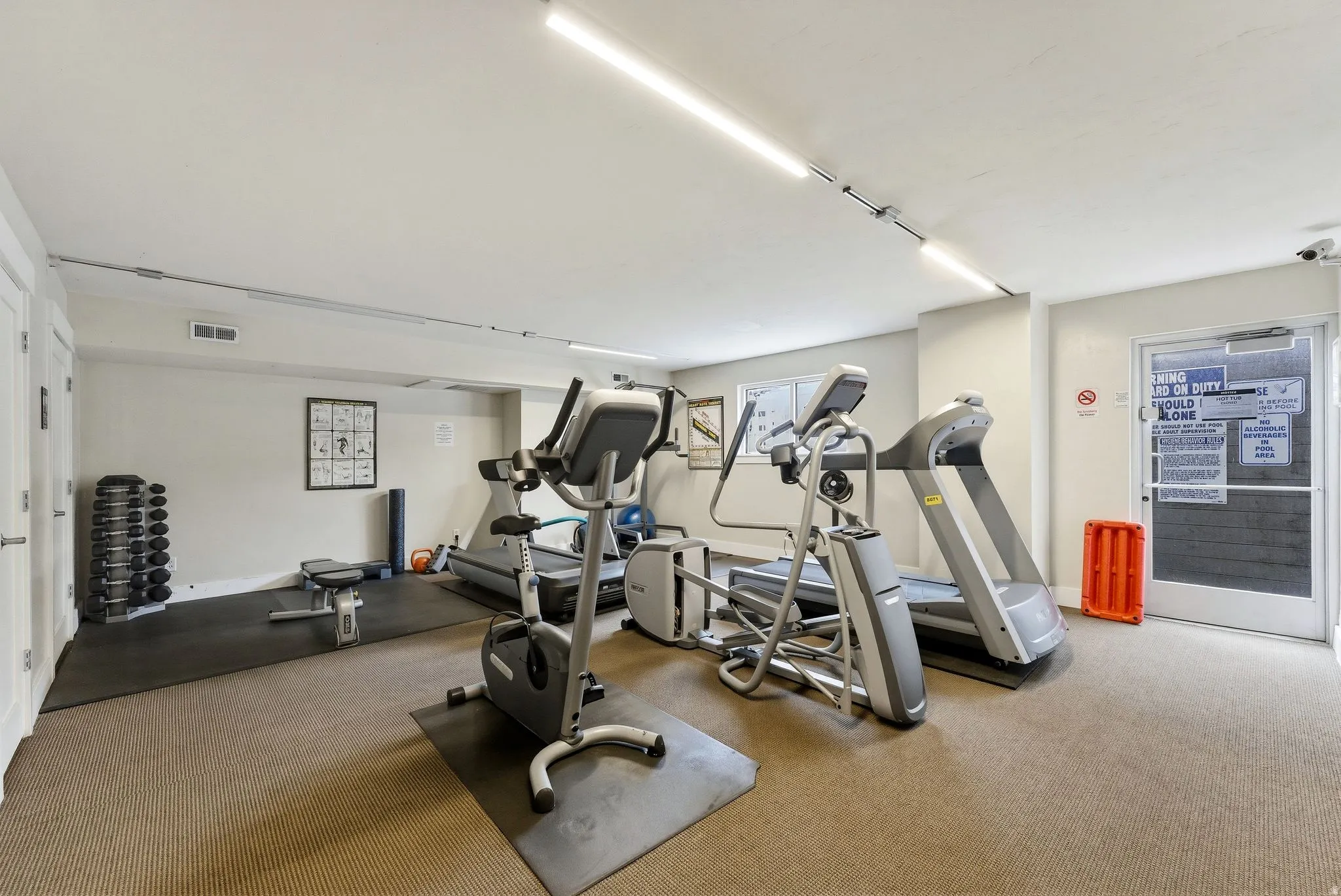 Dedicated fitness room featuring cardio machines, weight racks, and a rubber mat flooring section