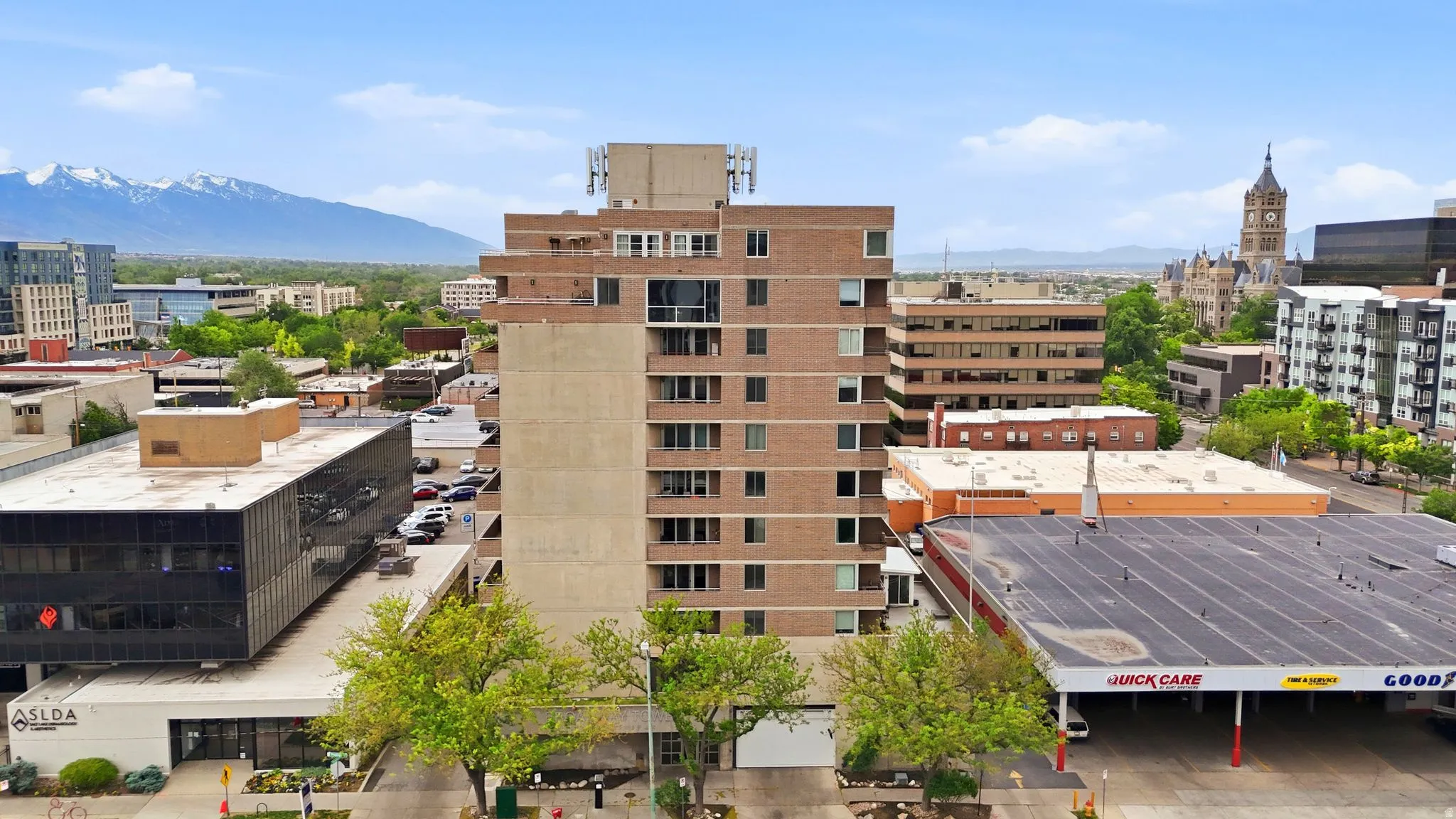 Multi-story building featuring a brick facade with multiple windows and balconies, surrounded by urban architecture