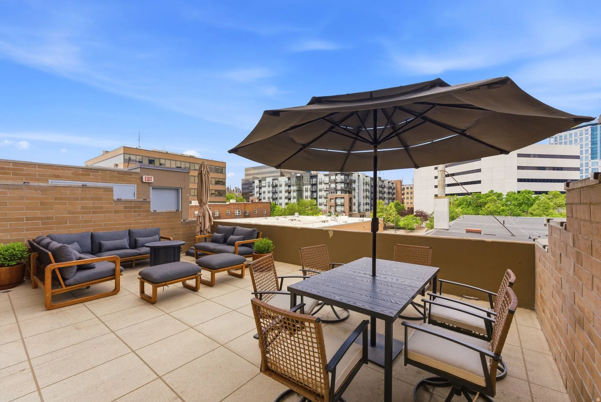 Expansive rooftop terrace featuring large format patio tiles, a brick perimeter wall, and distant city buildings