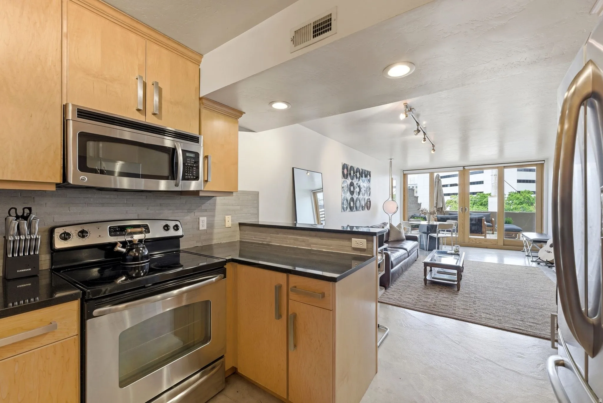 Kitchen featuring stainless steel appliances including an oven range and built-in microwave, wood-finish cabinetry, dark countertops, and a gray tile backsplash