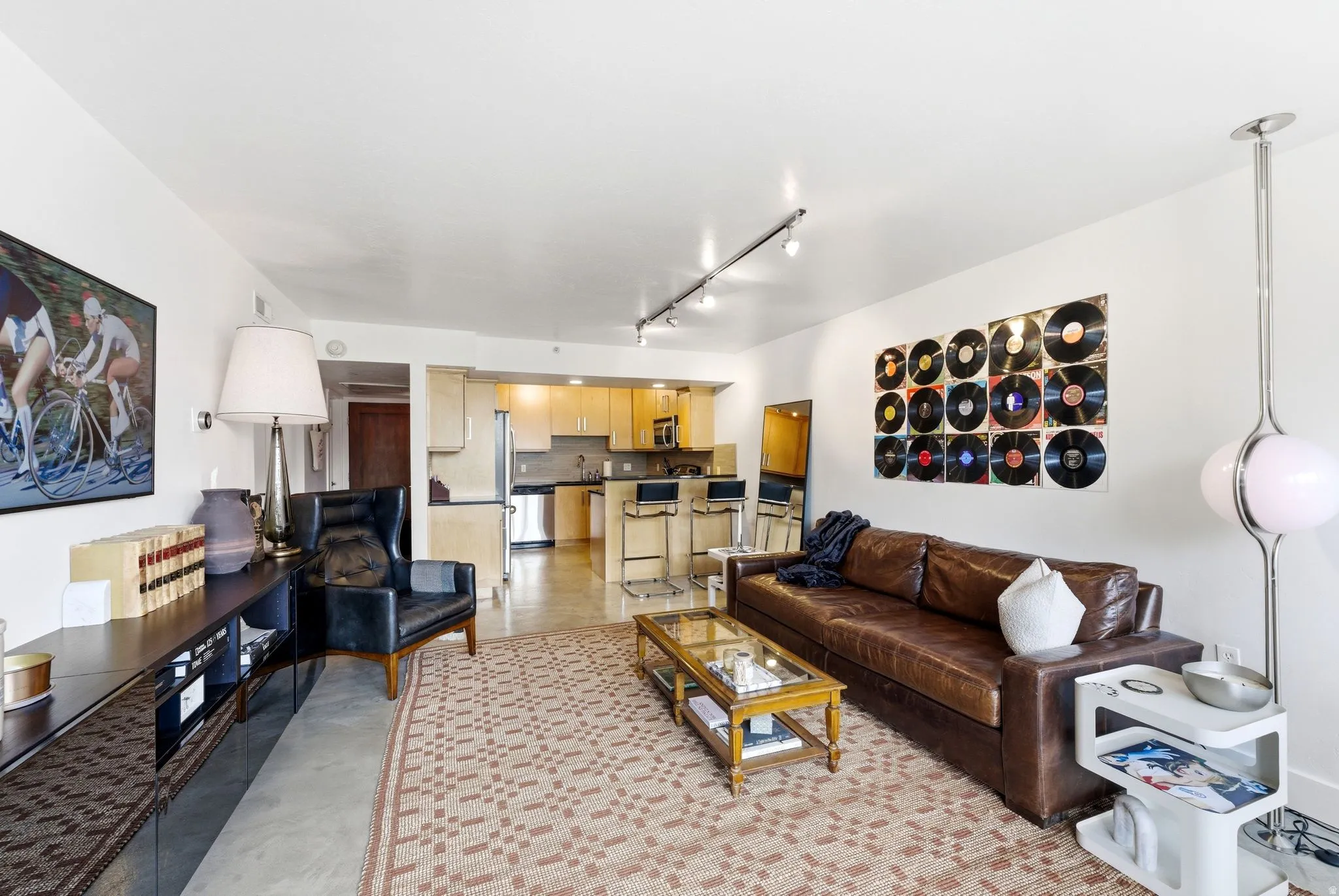 Open-concept living area featuring a kitchen with light wood cabinetry, stainless steel appliances, and dark countertops