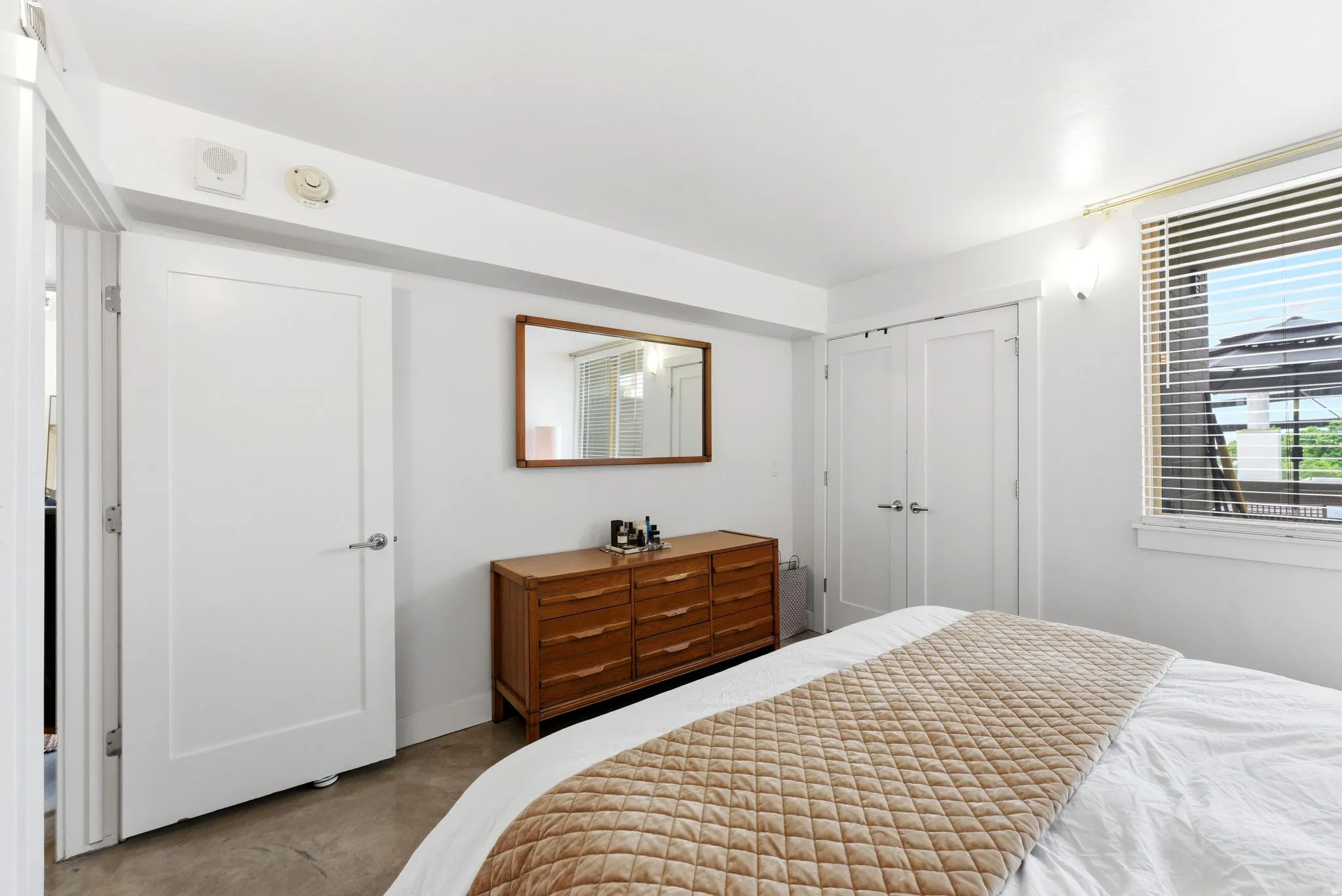 Room featuring a large window with horizontal blinds, a single white paneled door, and a double white paneled closet door