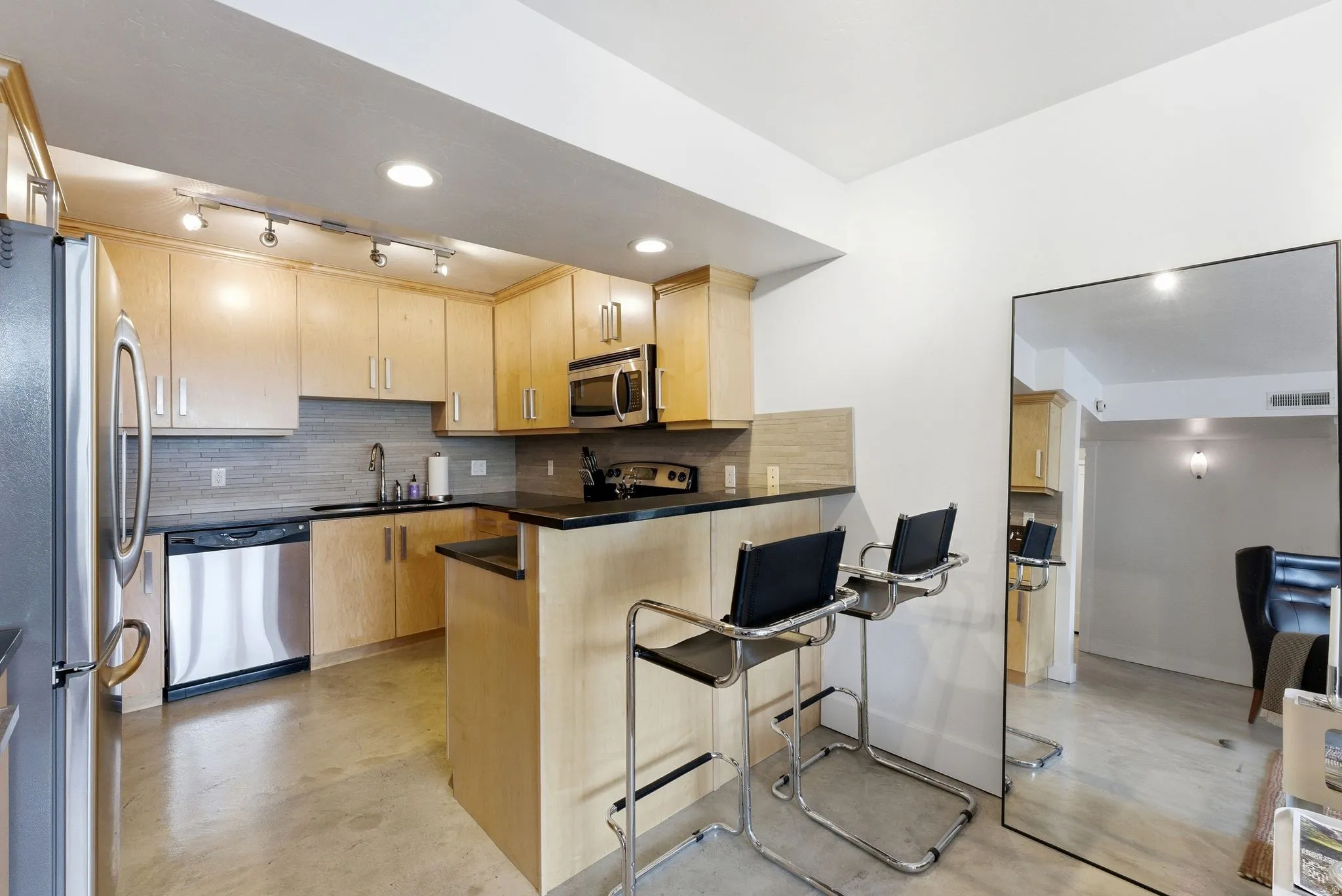 Kitchen featuring wood-finish cabinetry, black countertops, stainless steel appliances, and a gray tile backsplash